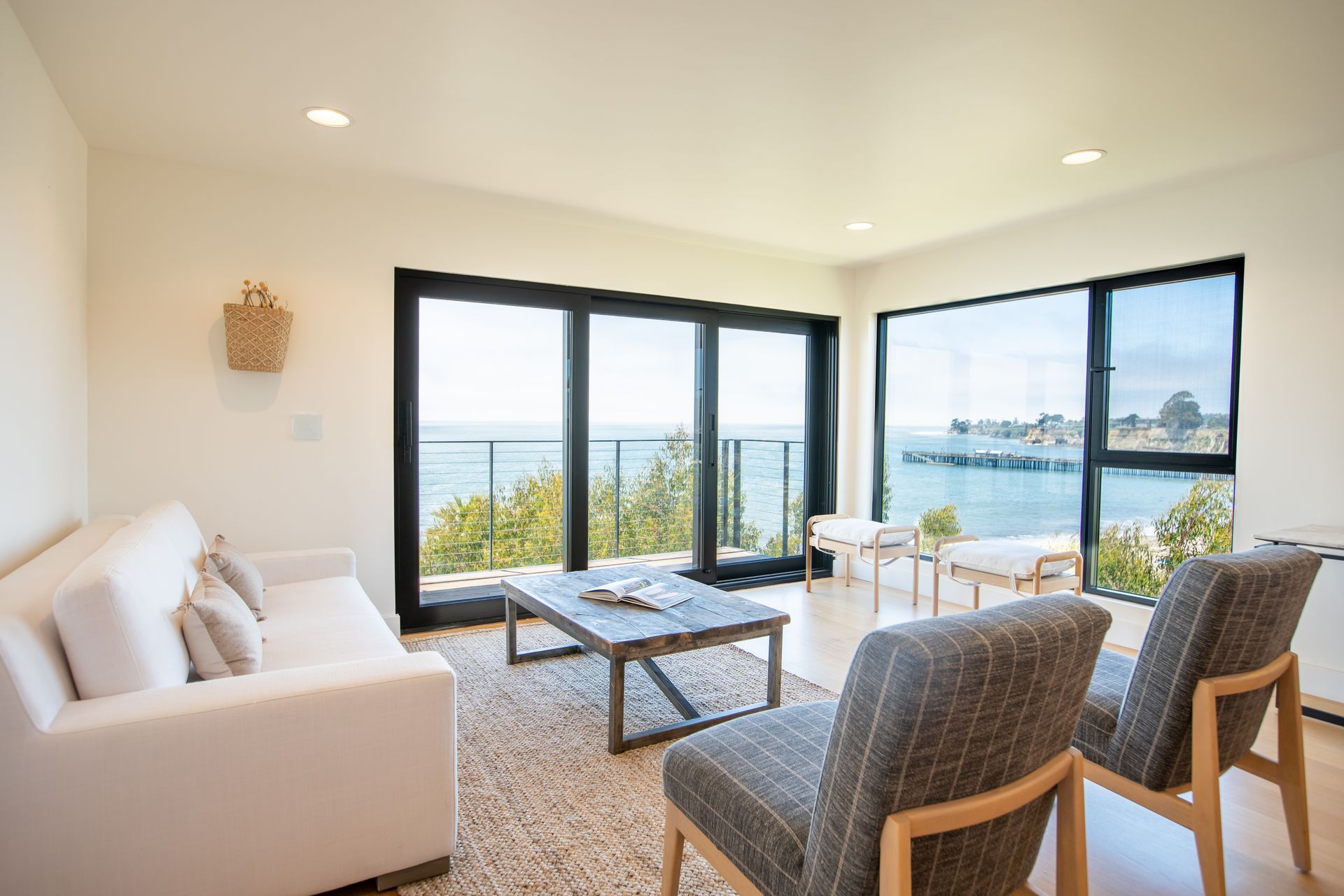 Bright modern living room with ocean views, beige sofa, wicker chairs, and glass coffee table
