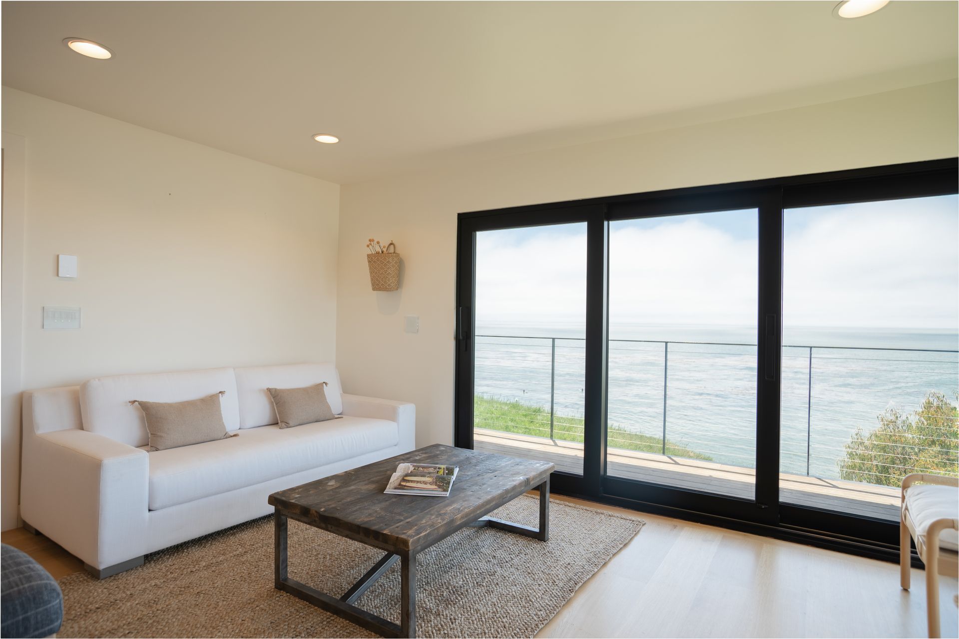 Bright living room with white sofa, coffee table, and large ocean-view windows