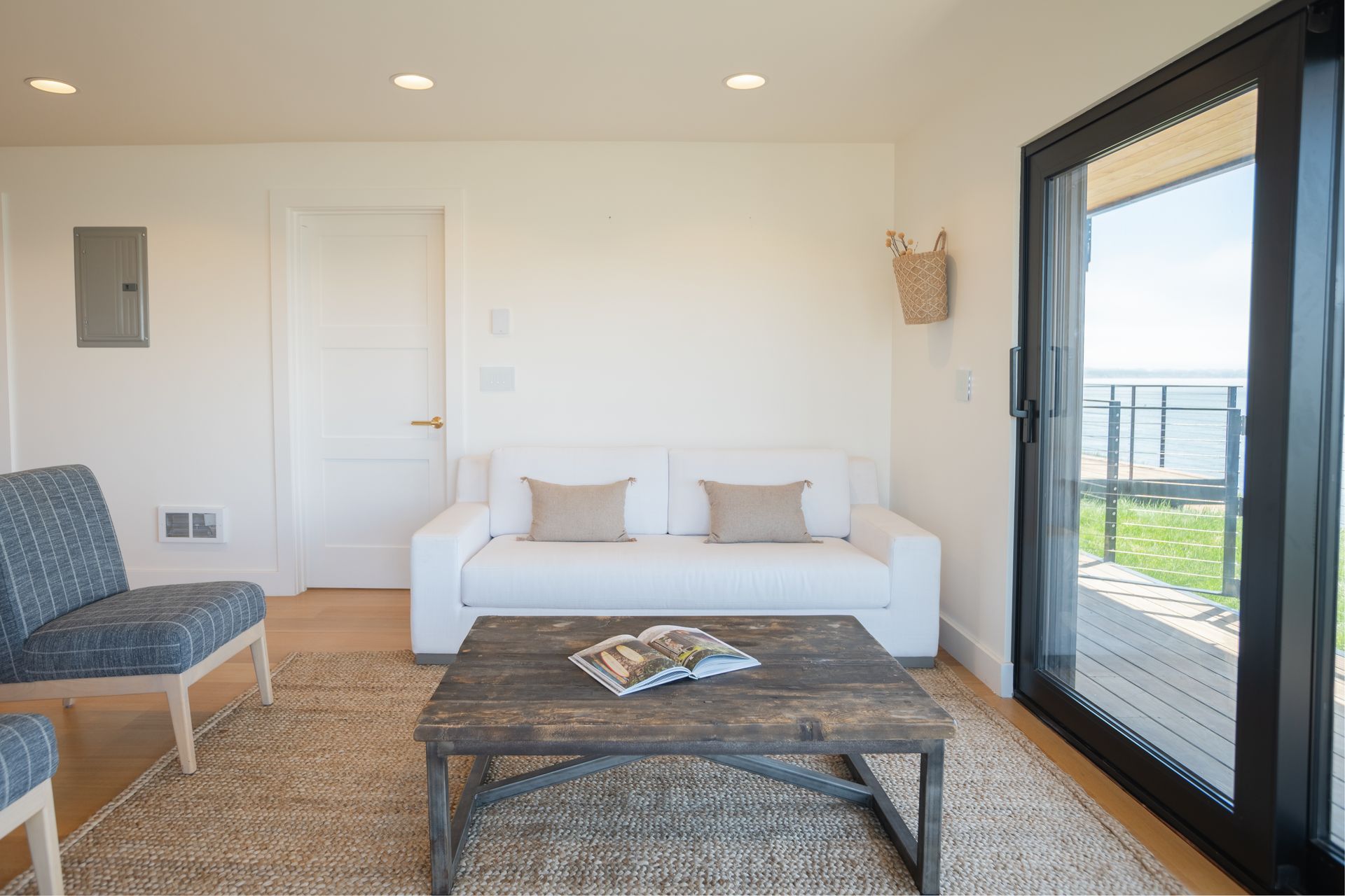 Bright living room with a white sofa, wood coffee table, chair, and large glass door to a balcony.