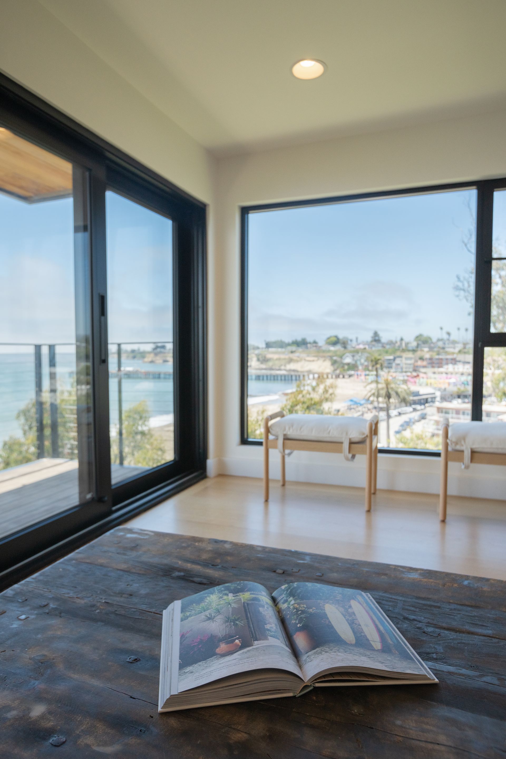 Bright modern room with ocean view, open book on rug, and two chairs by large windows