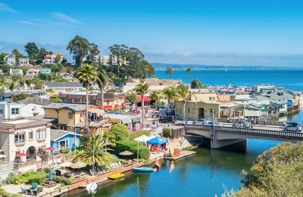 Colorful coastal town with boats, bridge, and blue bay under a clear sky