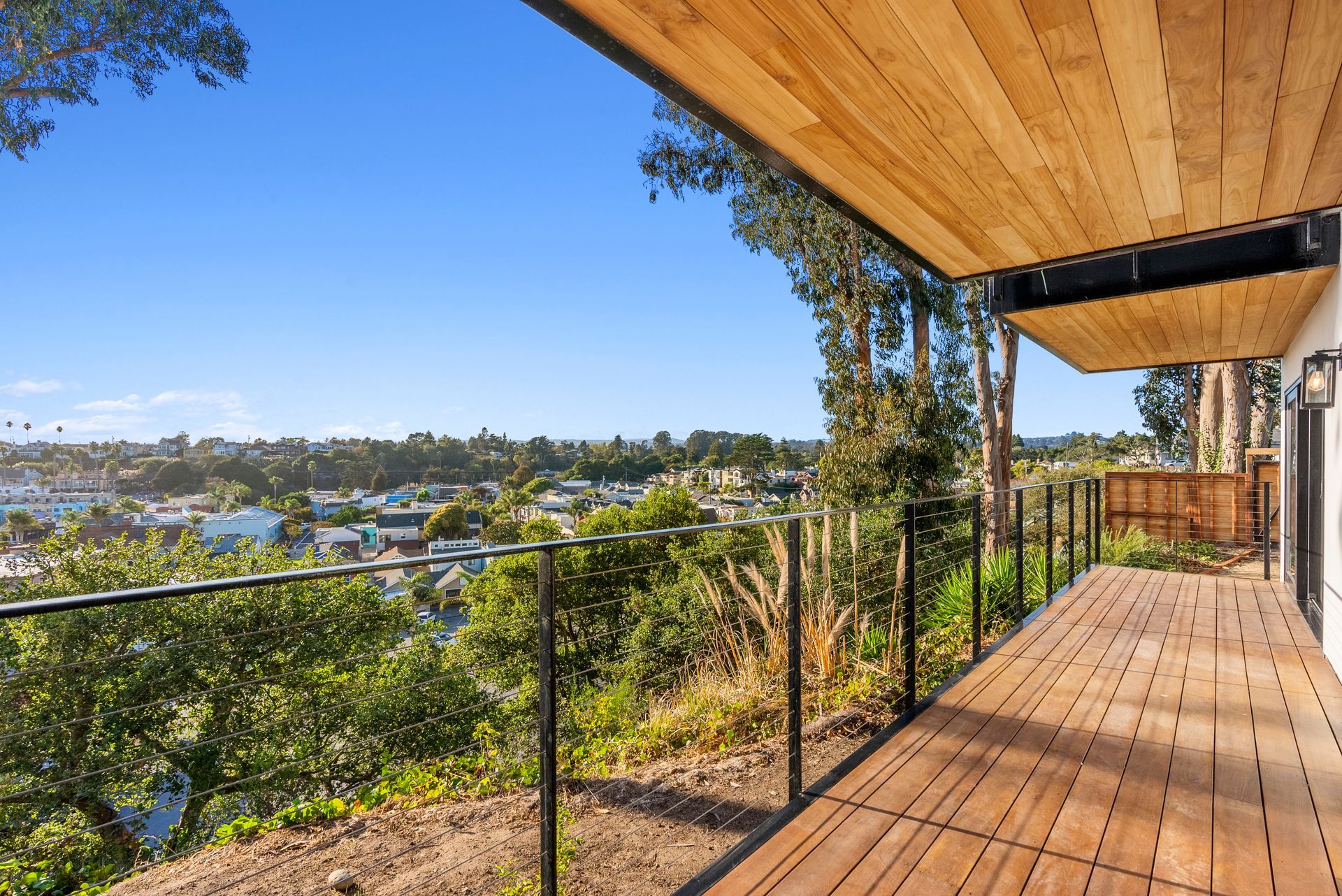 Wooden deck overlooking a lake and neighborhood, with black railing, trees, and clear blue sky