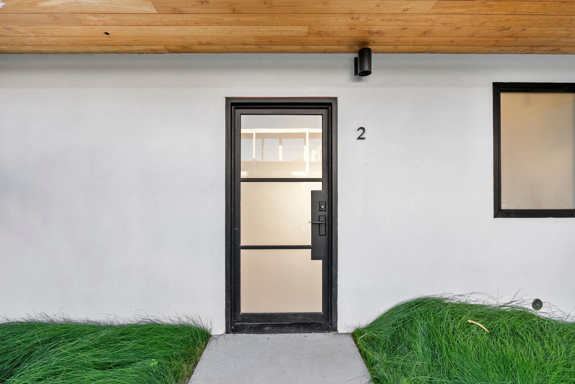 Front entrance with a black-framed glass door, beige wall, house number 2, and grass on both sides of a walkway