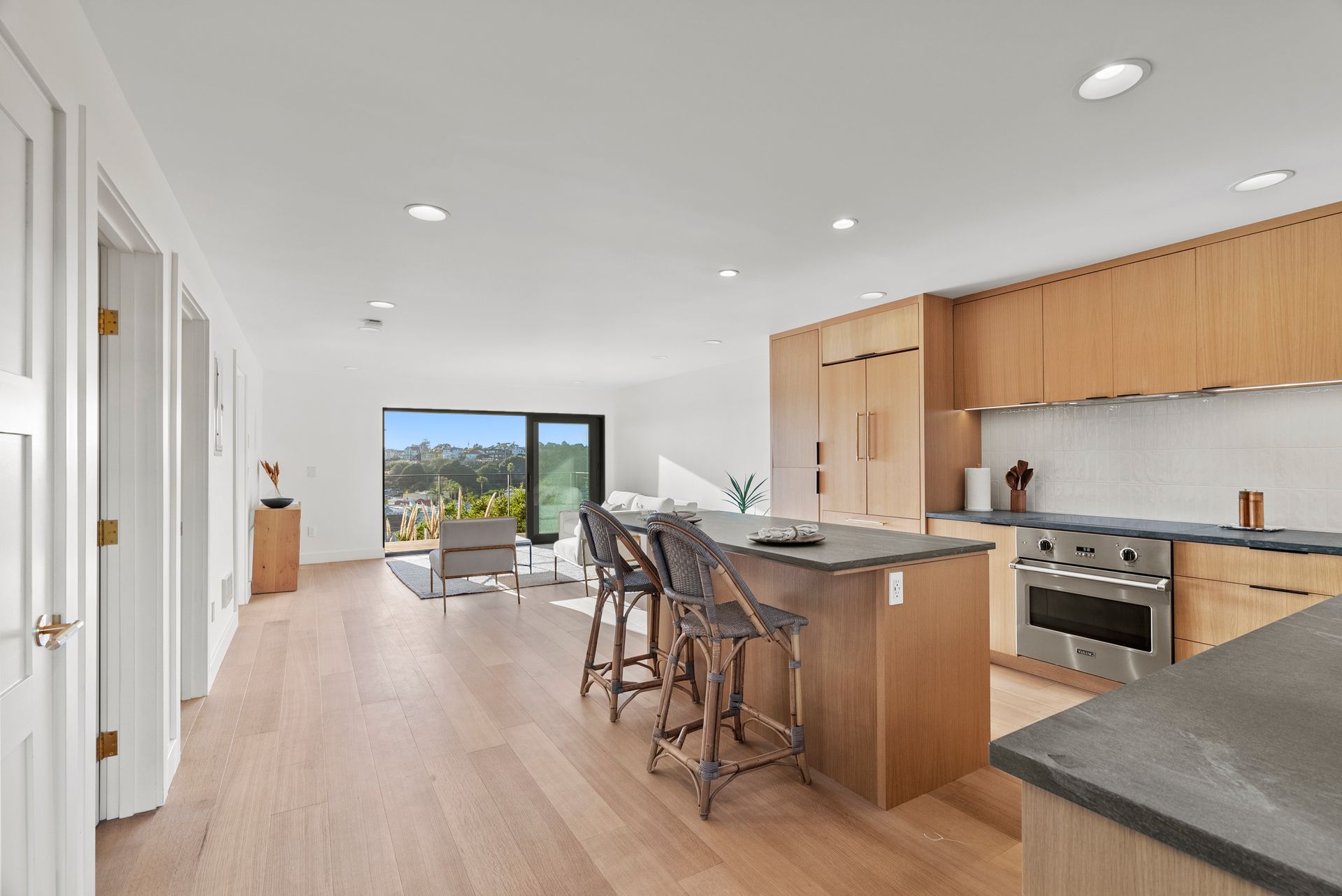 Modern open-plan kitchen and living area with wood cabinets, island seating, and large sliding glass doors