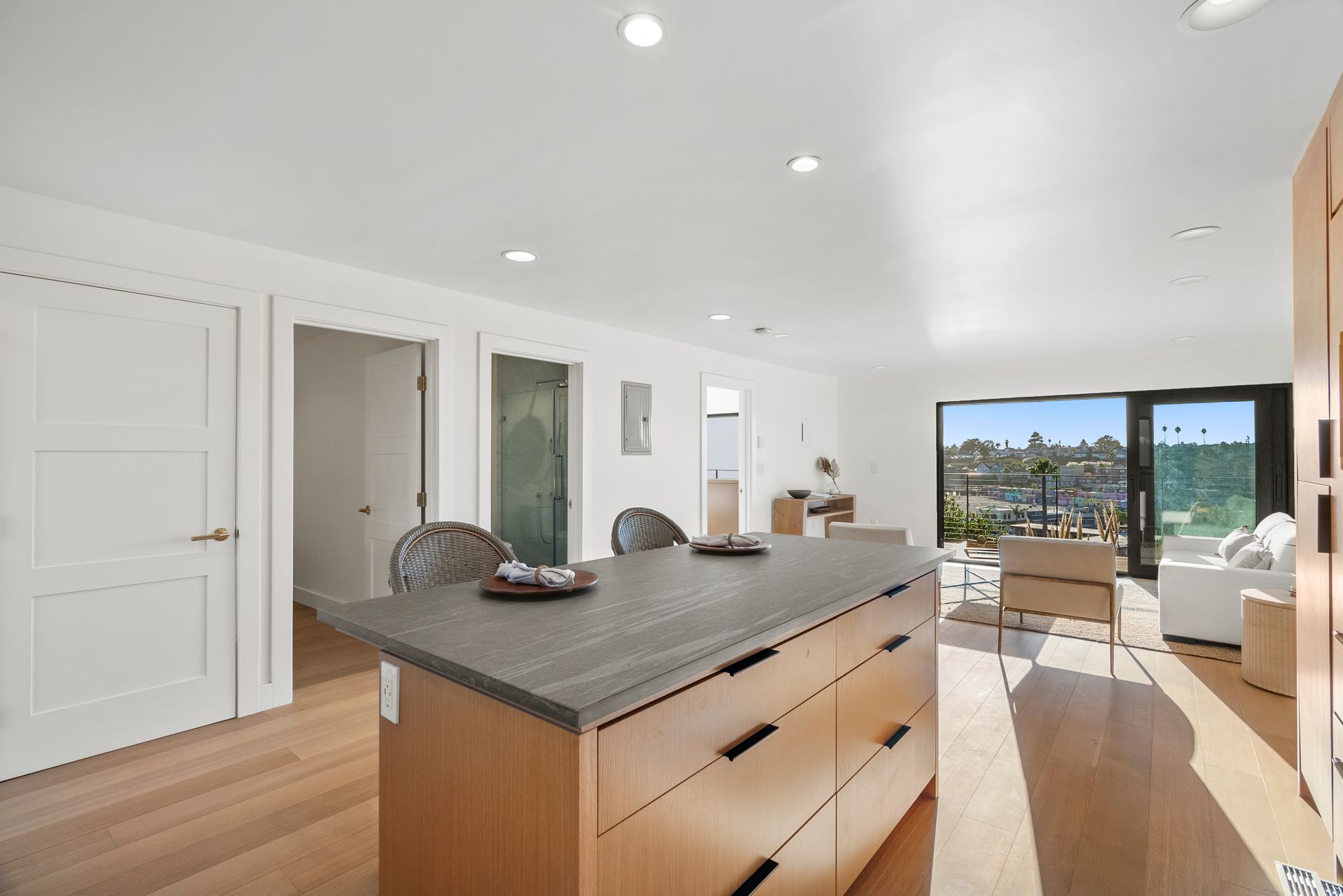 Bright modern kitchen with island, white walls, wood floors, and sliding doors opening to a patio and ocean view