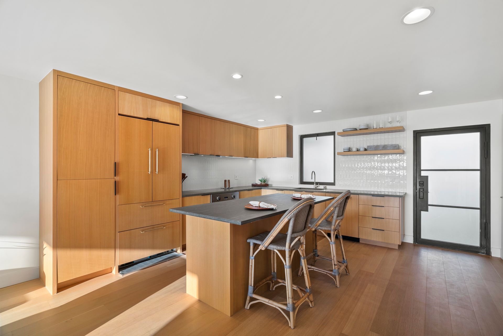 Modern kitchen with wood cabinets, island, bar stools, and white walls and floor-to-ceiling cabinets