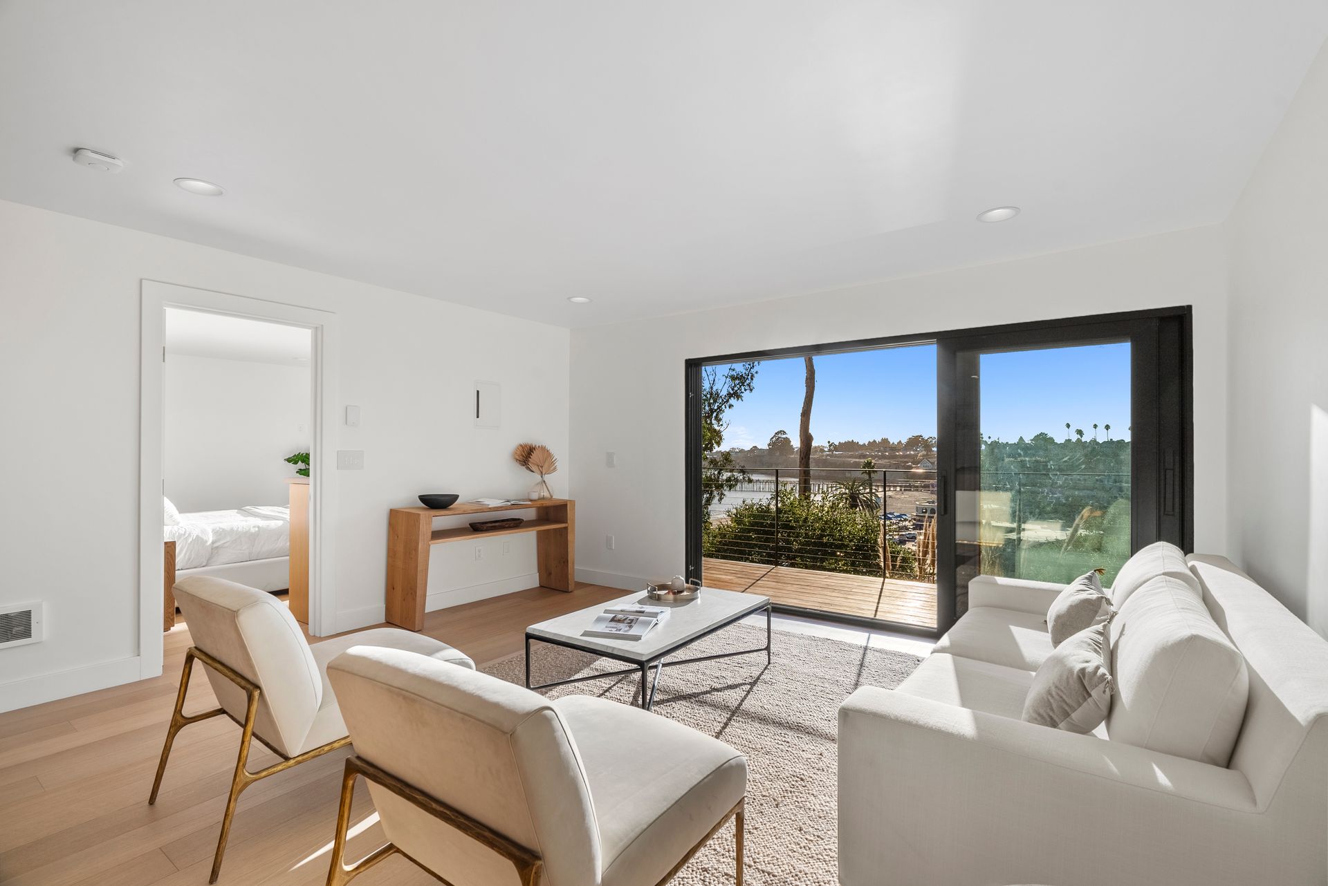Bright modern living room with white sofa, chairs, rug, wooden console, and large sliding glass doors to a terrace.