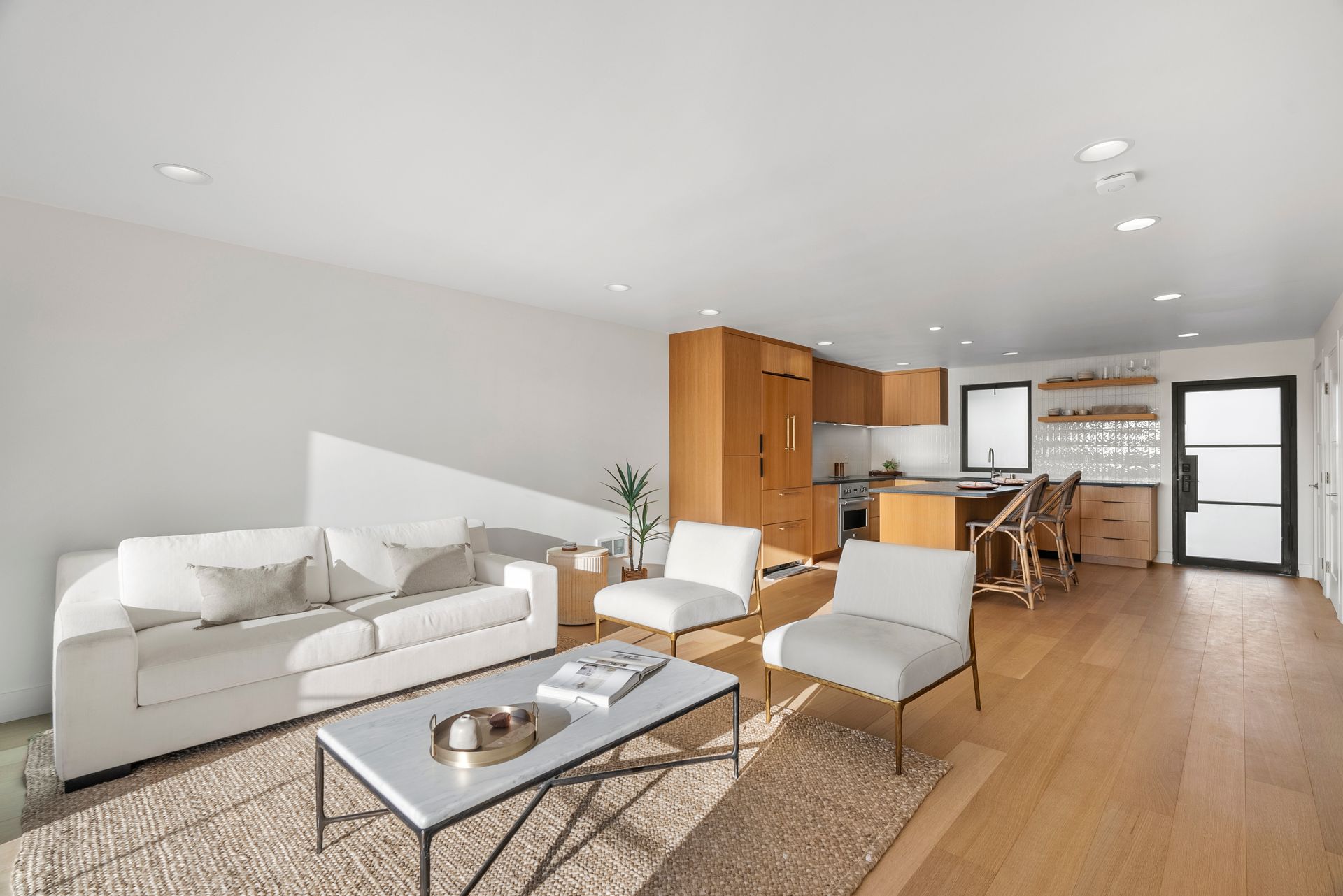 Bright modern open-plan living room with white sofa, coffee table, and kitchen-dining area in back