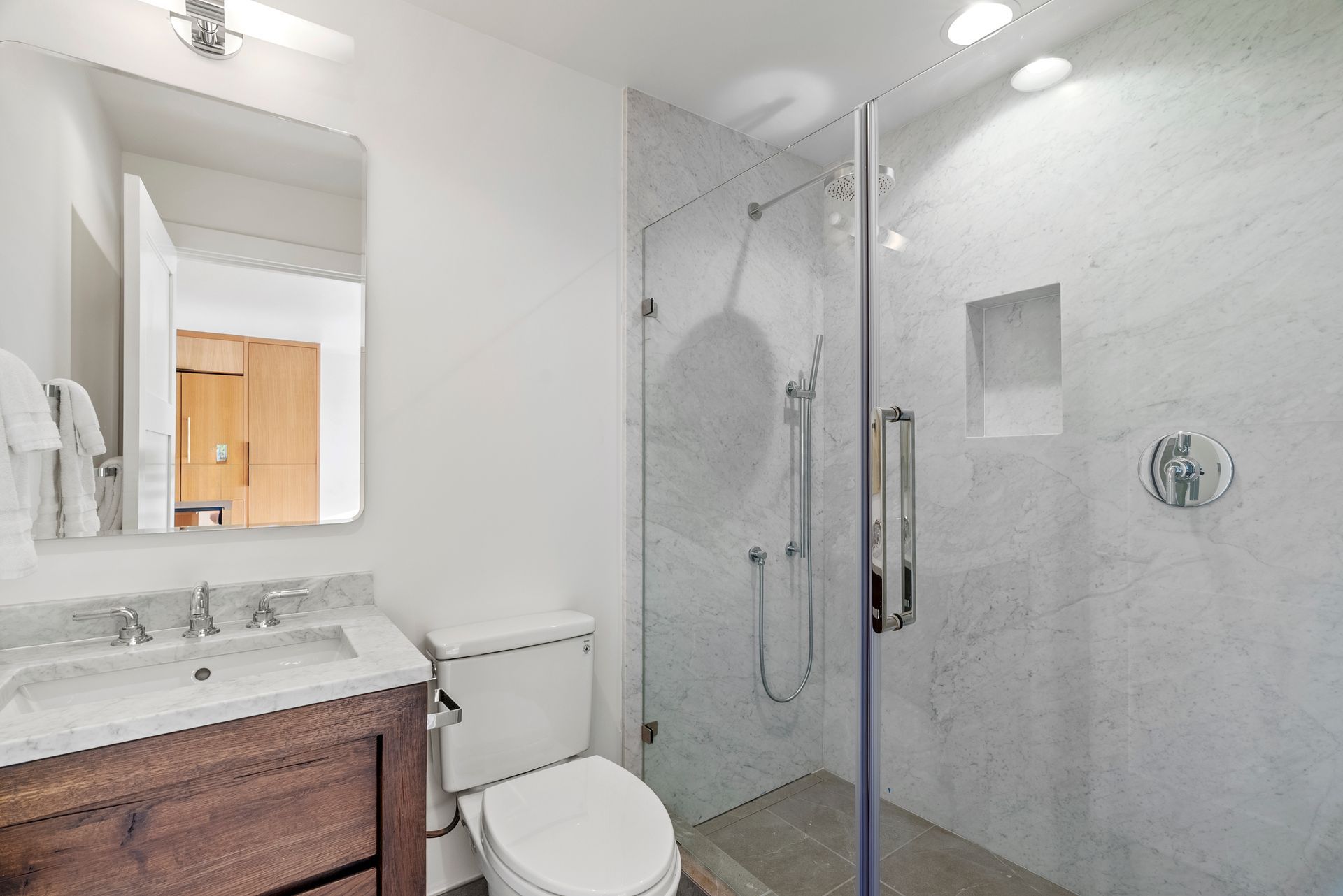Modern bathroom with vanity, toilet, and glass-enclosed marble shower.