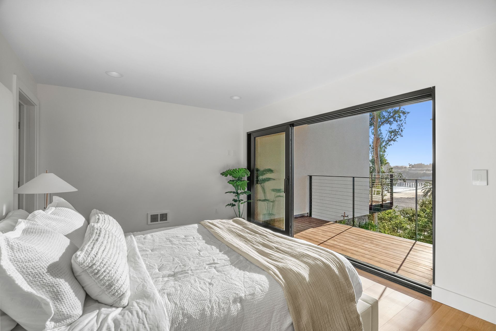 Bright bedroom with white bedding and open glass doors to a sunny patio and garden view