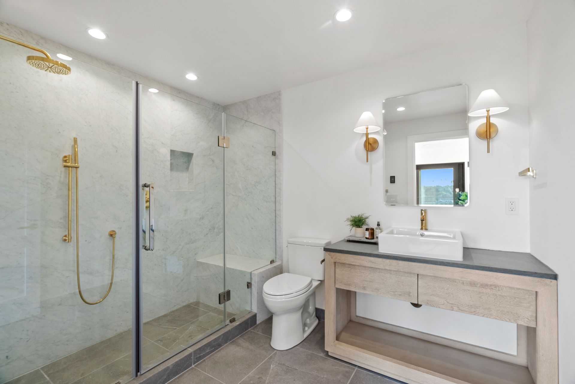 Modern bathroom with glass shower, toilet, and vanity with mirror and gold fixtures