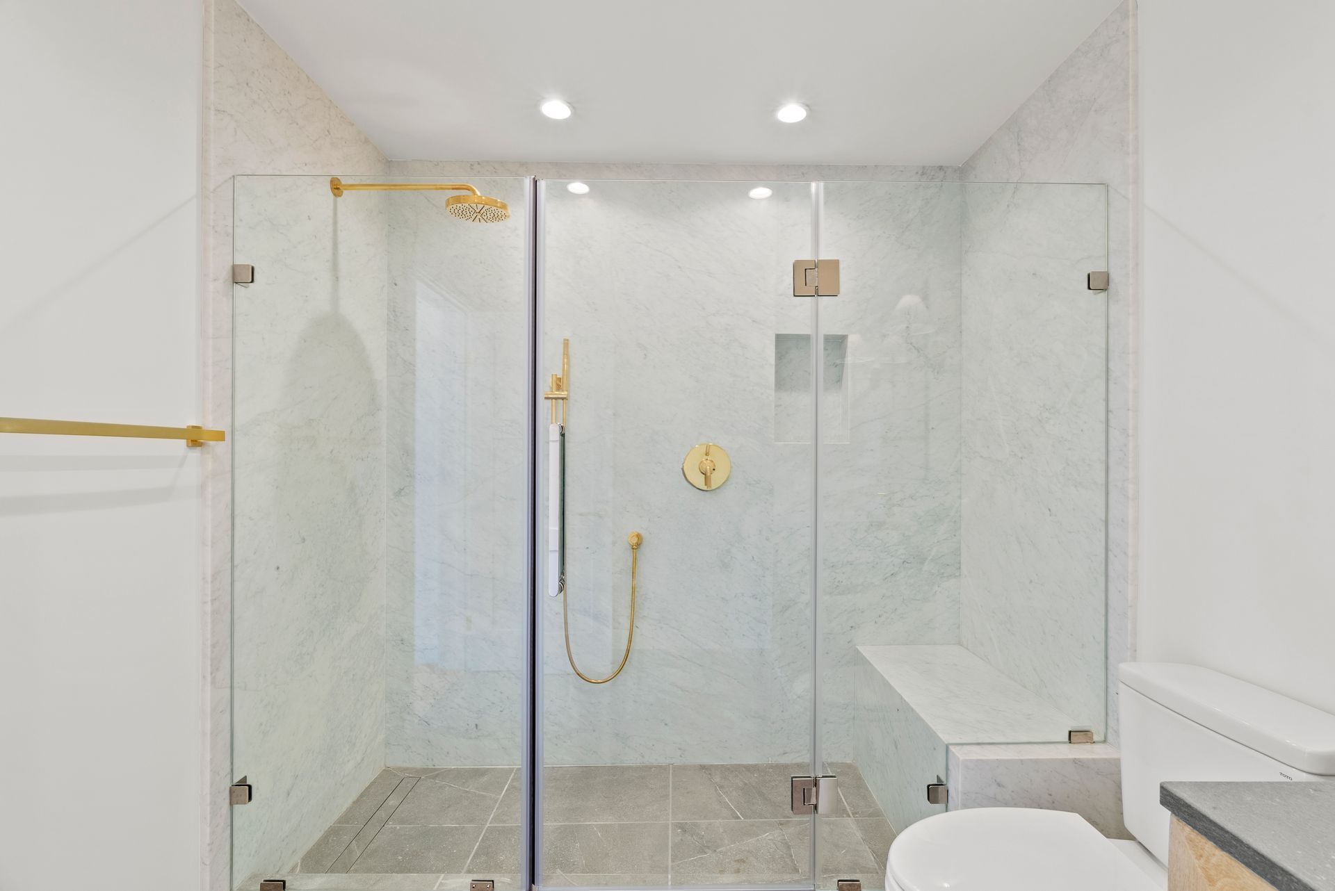 Modern white-tiled shower with glass doors, gold fixtures, and a built-in bench.