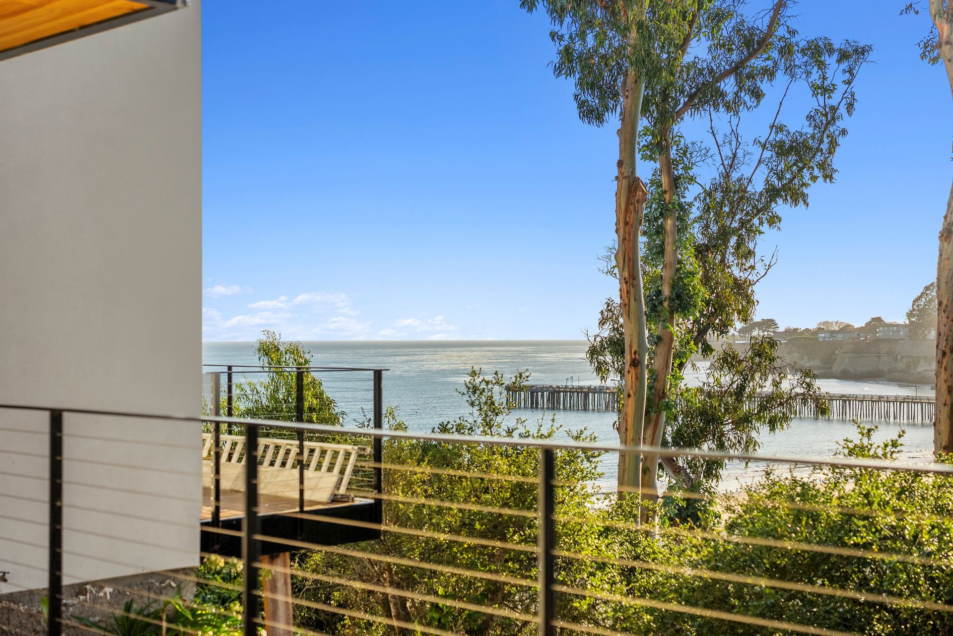 Balcony view of a lake and pier beyond a railing, with trees and a bright blue sky.