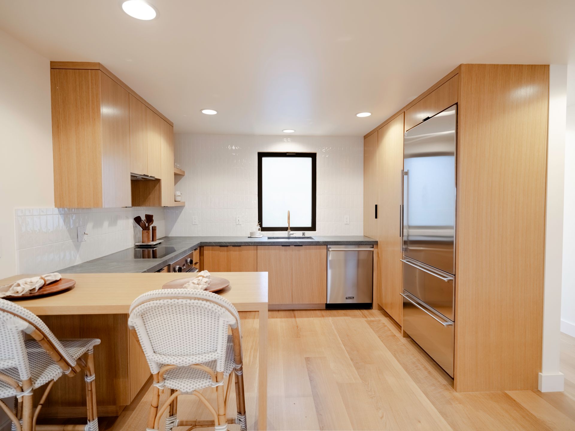 Modern kitchen with light wood cabinets, island seating, stainless appliances, and a central window