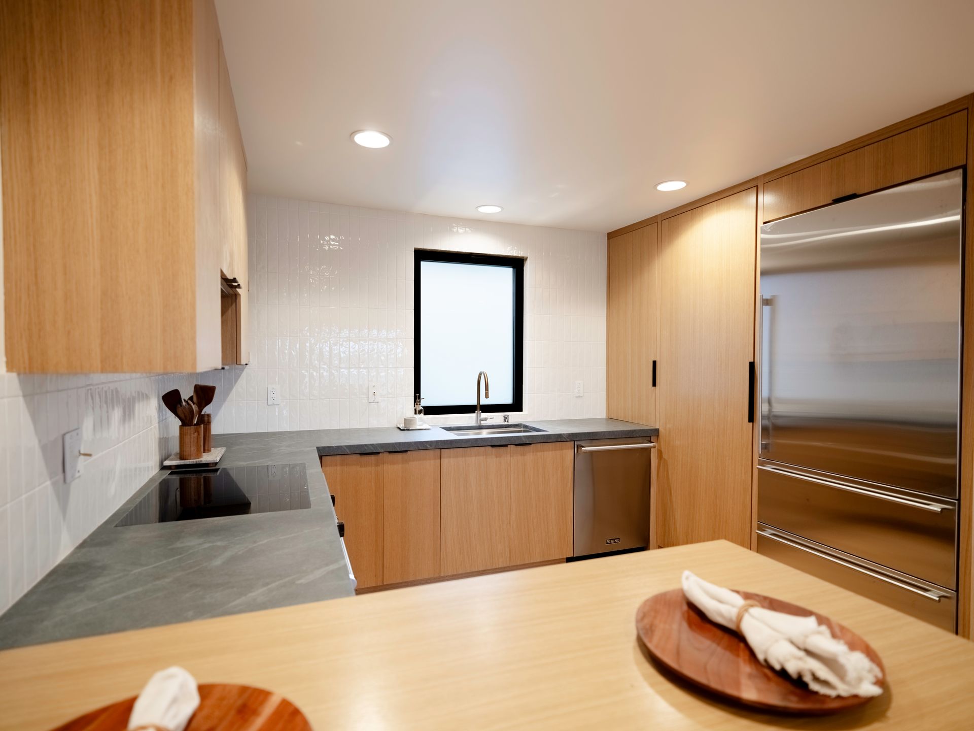 Modern kitchen with wood cabinets, stainless appliances, black countertops, and a dining table in the foreground
