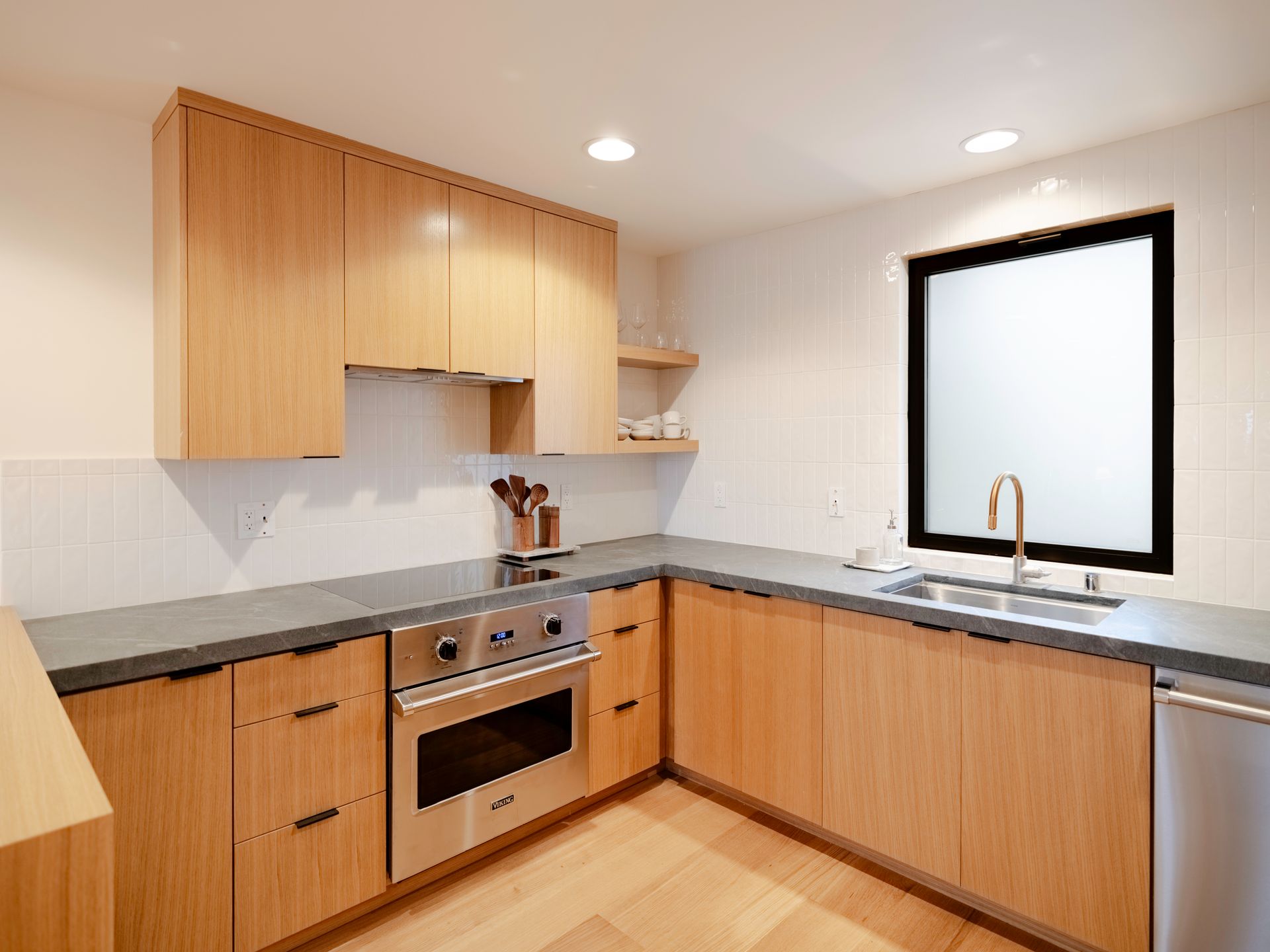 Modern kitchen with light wood cabinets, gray countertops, and a large window over the sink