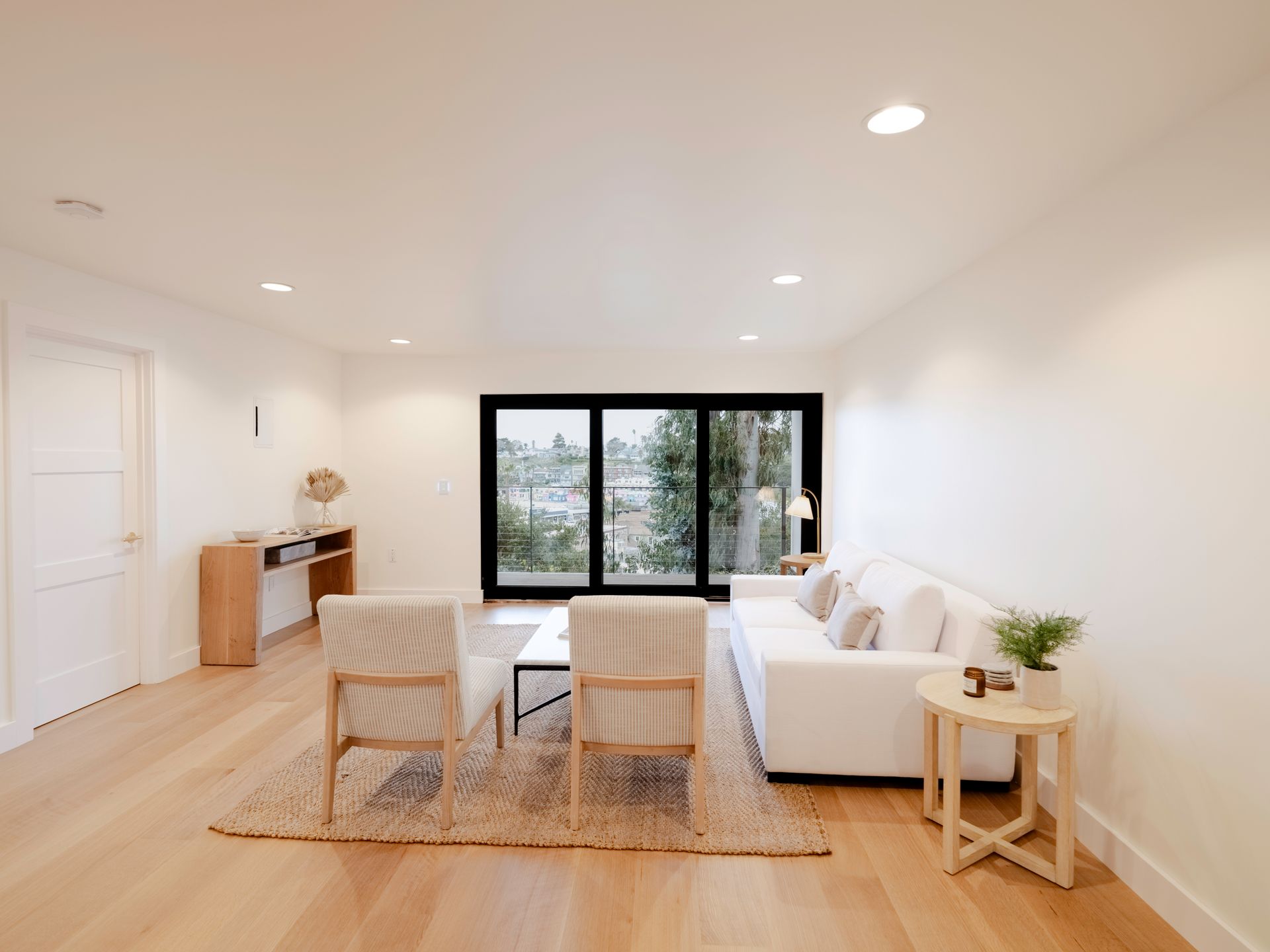 Bright minimalist living room with white sofa, woven chairs, rug, and large black-framed windows