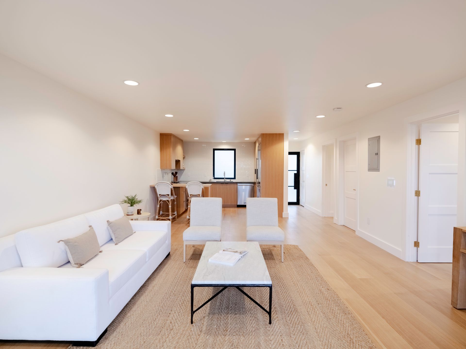 Bright open living room with white sofa, coffee table, dining area, and kitchen in the background