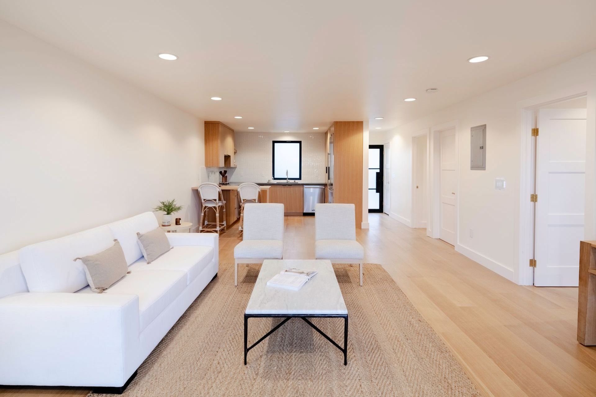 Bright open living room with white sofa, coffee table, dining area, and kitchen in the background