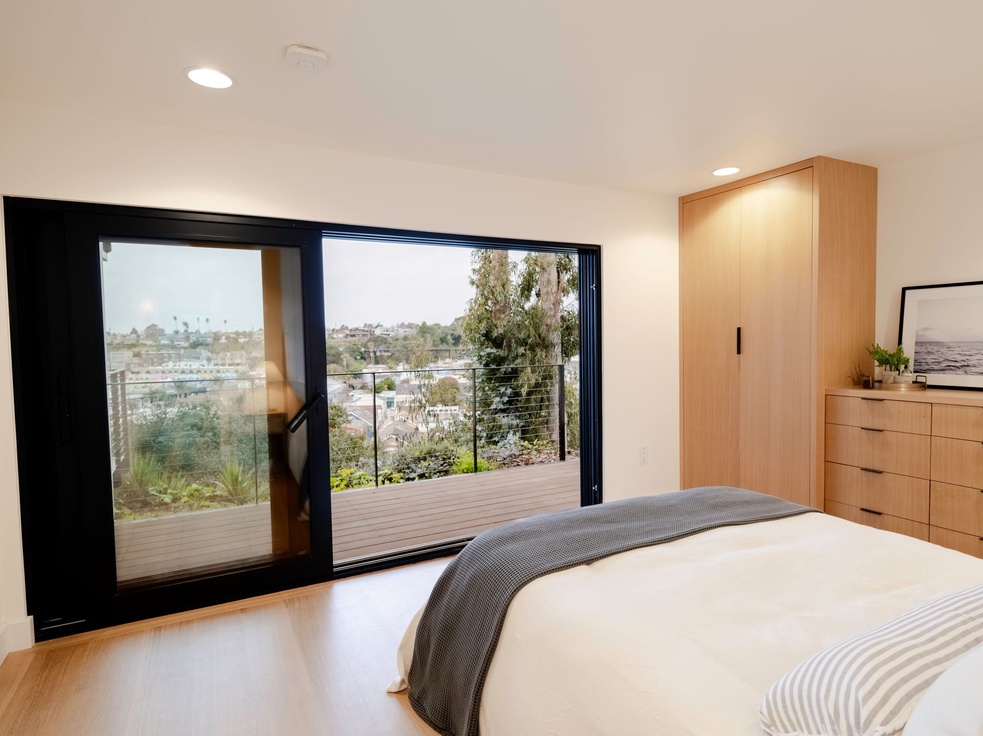 Modern bedroom with large sliding doors, city-view balcony, and light wood furniture