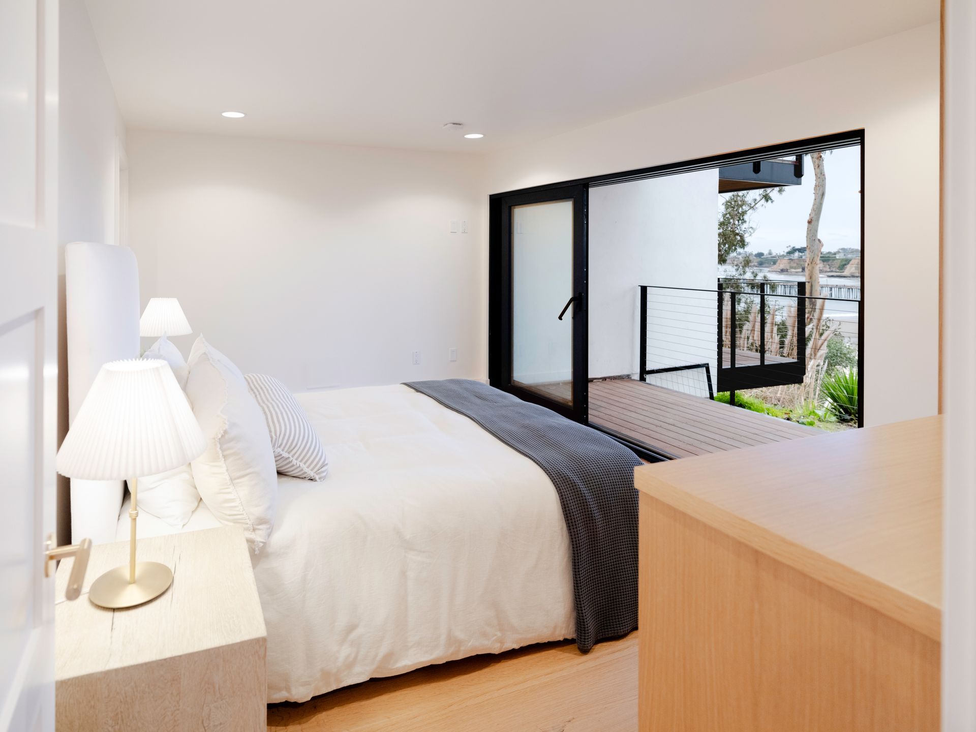 Bright minimalist bedroom with white bedding and open sliding doors to a balcony and ocean view