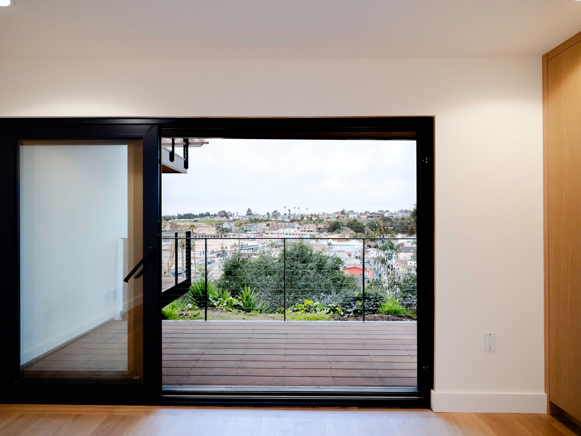 Sliding glass doors open to a wooden balcony with city and greenery views.