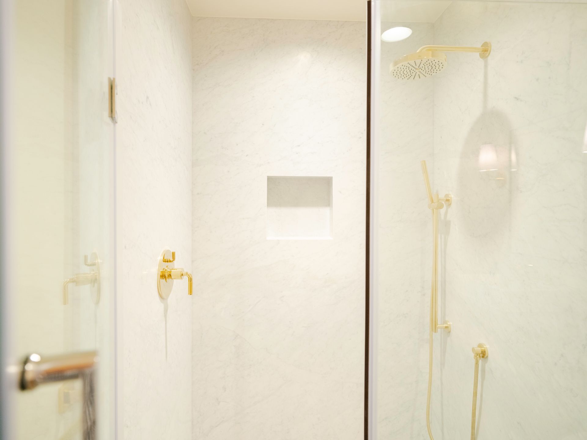 White bathroom shower stall with gold fixtures and a glass door handle
