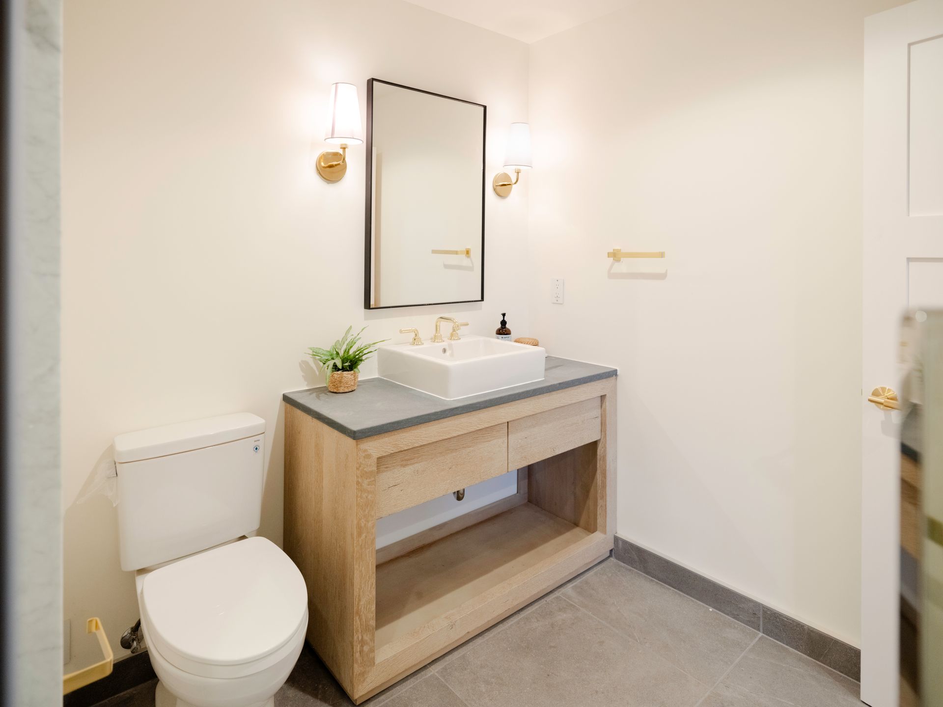 Modern bathroom vanity with wood cabinet, white sink, mirror, toilet, and wall sconces