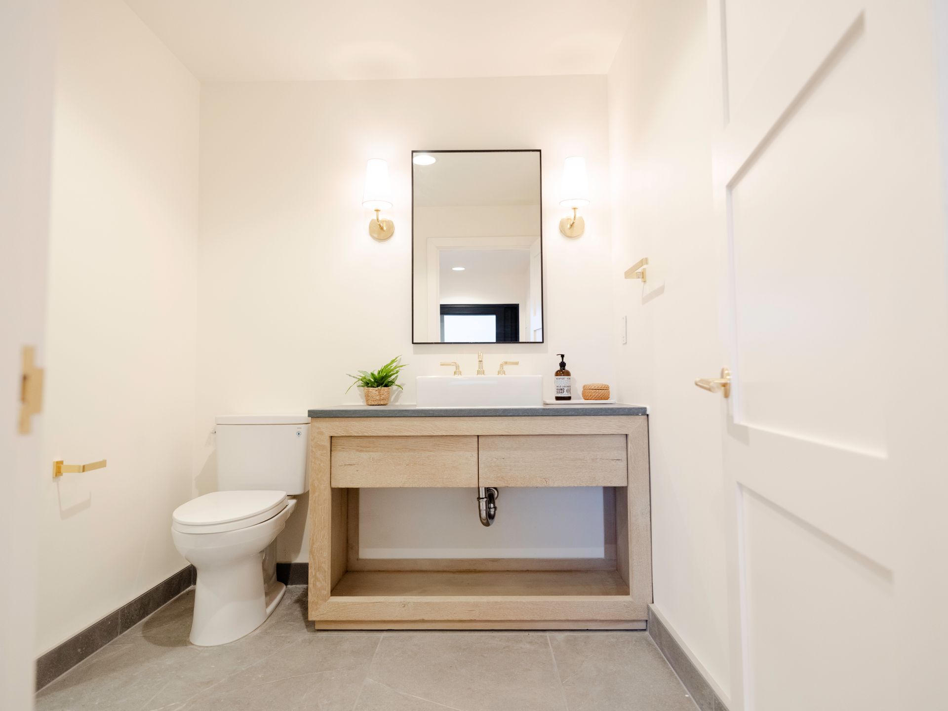Modern white bathroom with toilet, wood vanity, mirror, and wall sconces