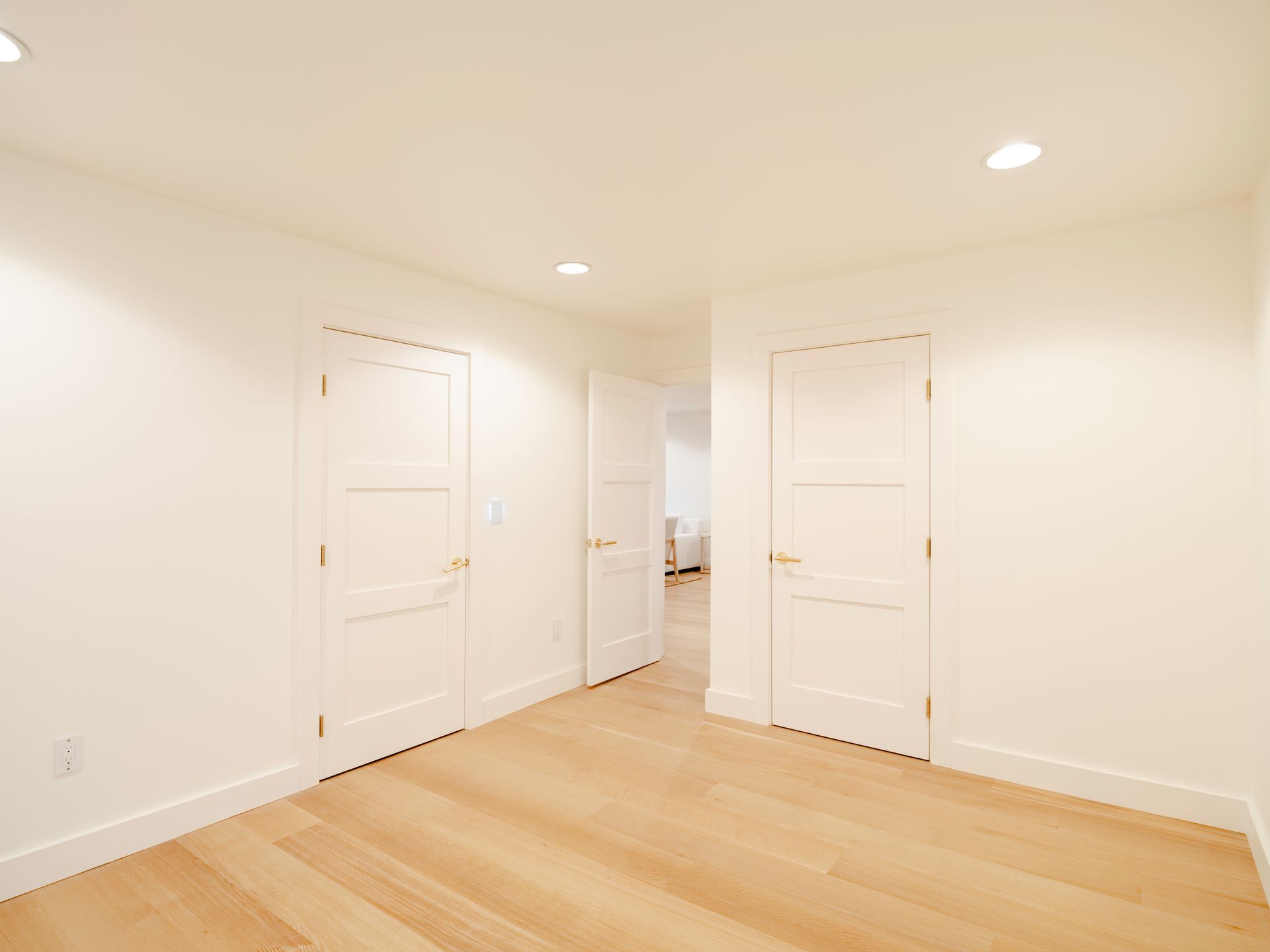 Empty beige bedroom with white doors, recessed ceiling lights, and light wood flooring