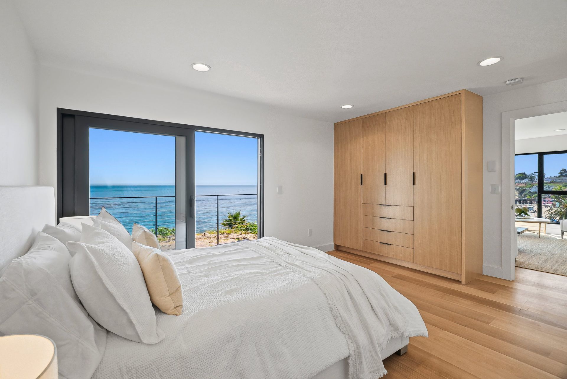 Bright bedroom with a large bed, wood closet, and ocean-view windows and balcony.
