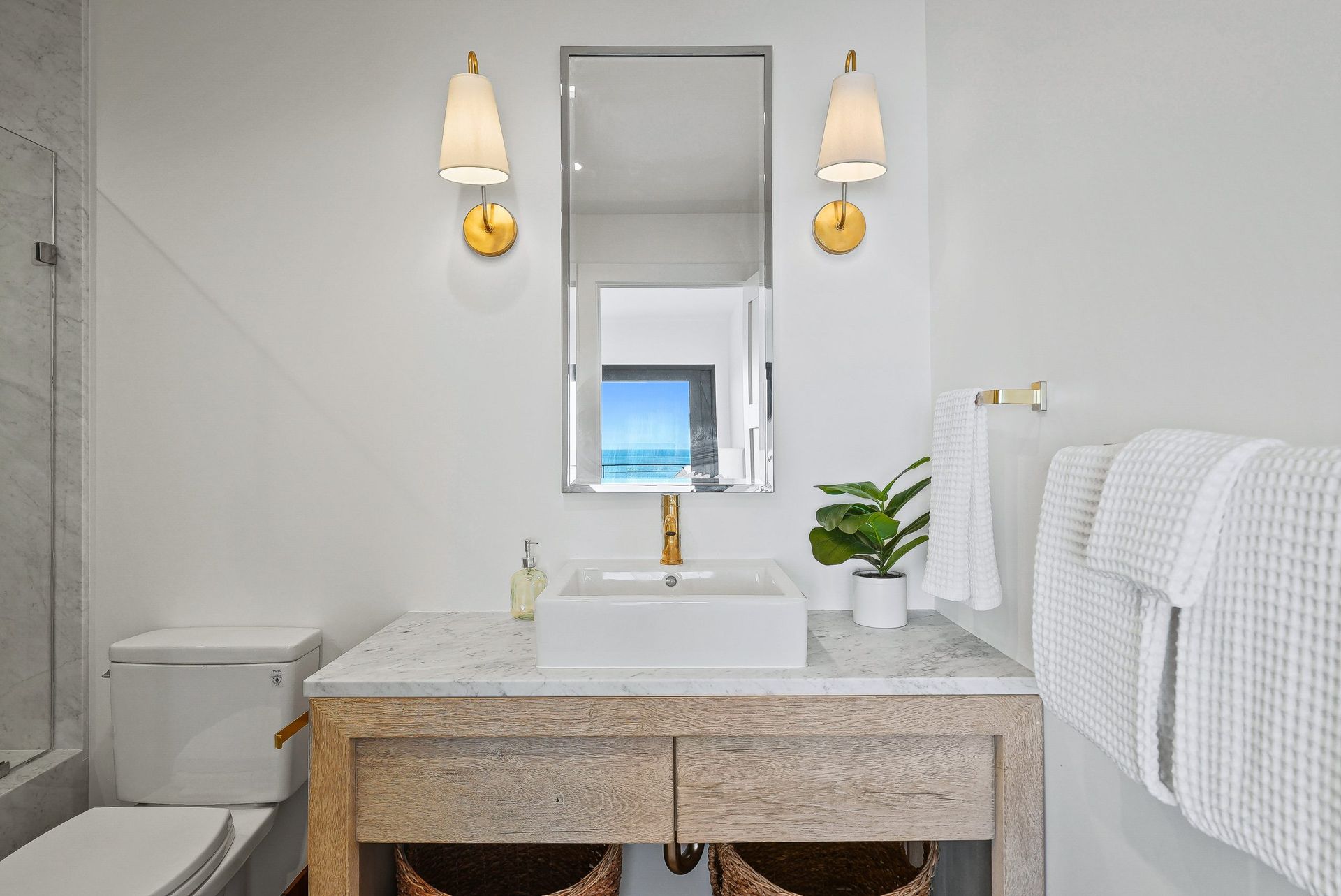 Bright bathroom with double vanity, wall mirror, sconces, and white towels
