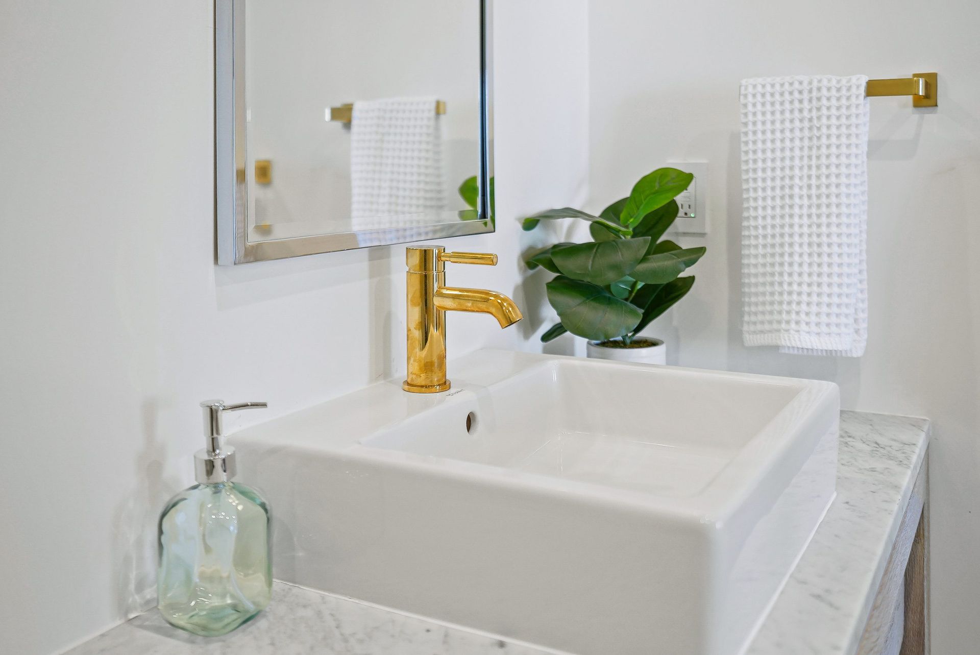 Modern bathroom sink with gold faucet, mirror, soap dispenser, and green plant pot