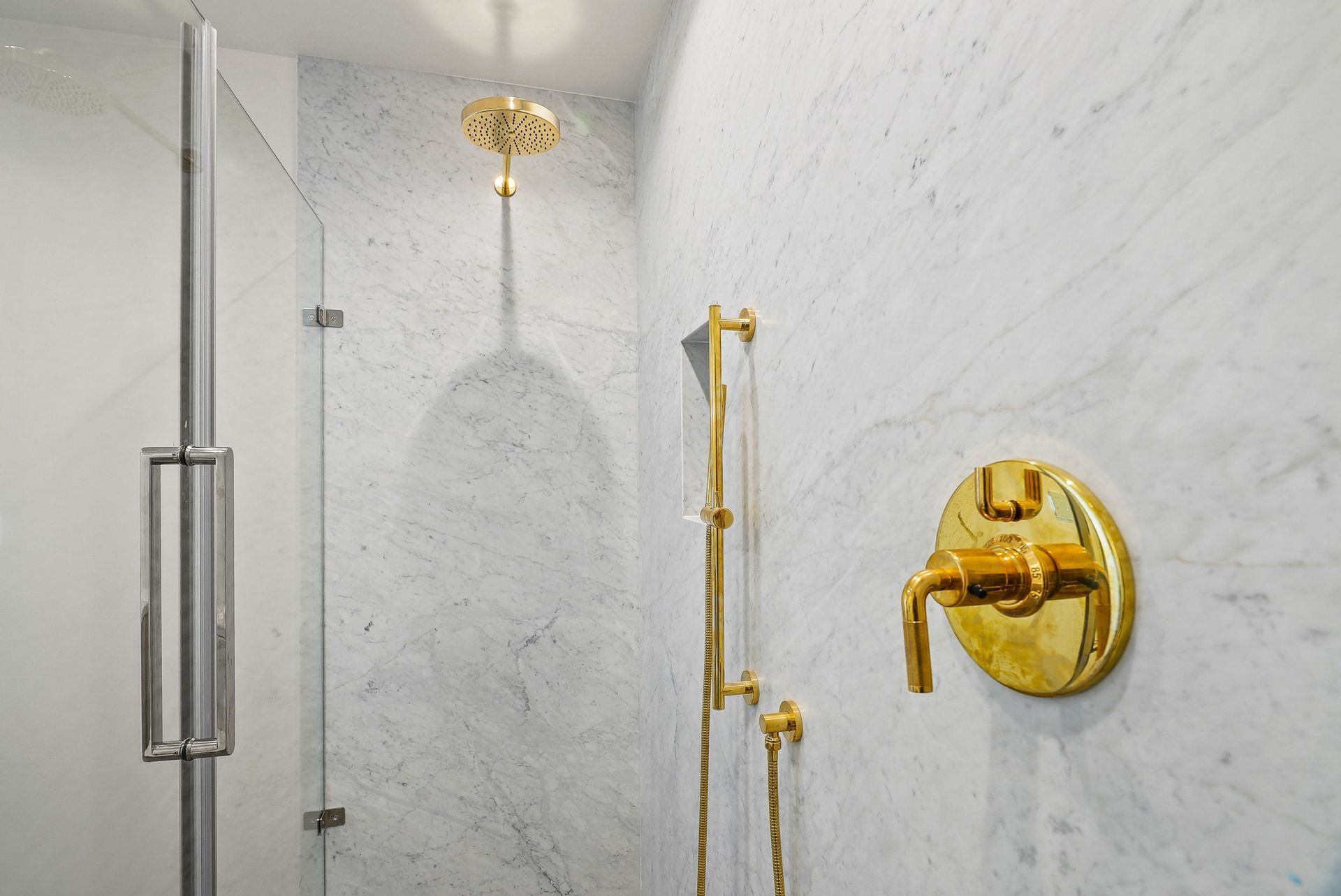 Marble shower with glass door, gold fixtures, and wall-mounted controls