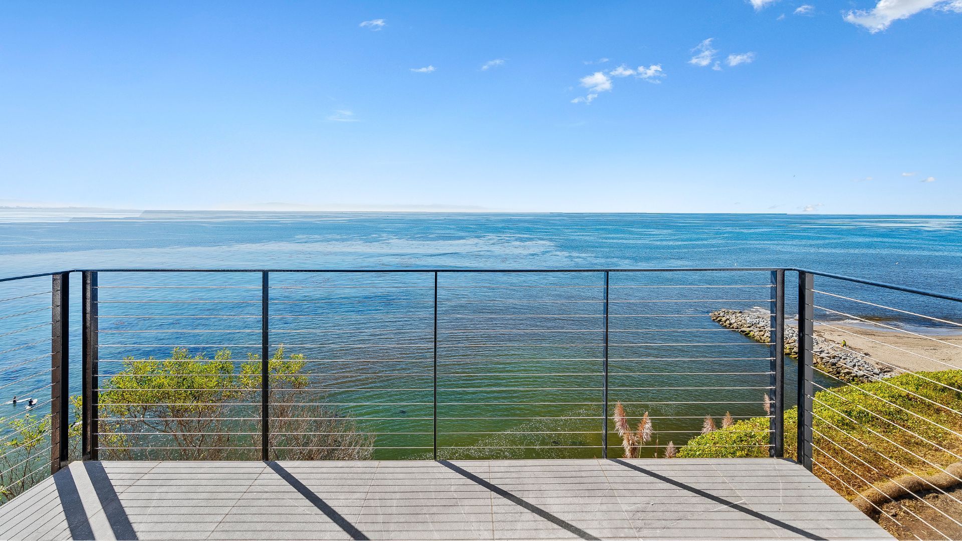 Balcony overlooking a calm blue ocean under a clear sky, with a glass railing in the foreground