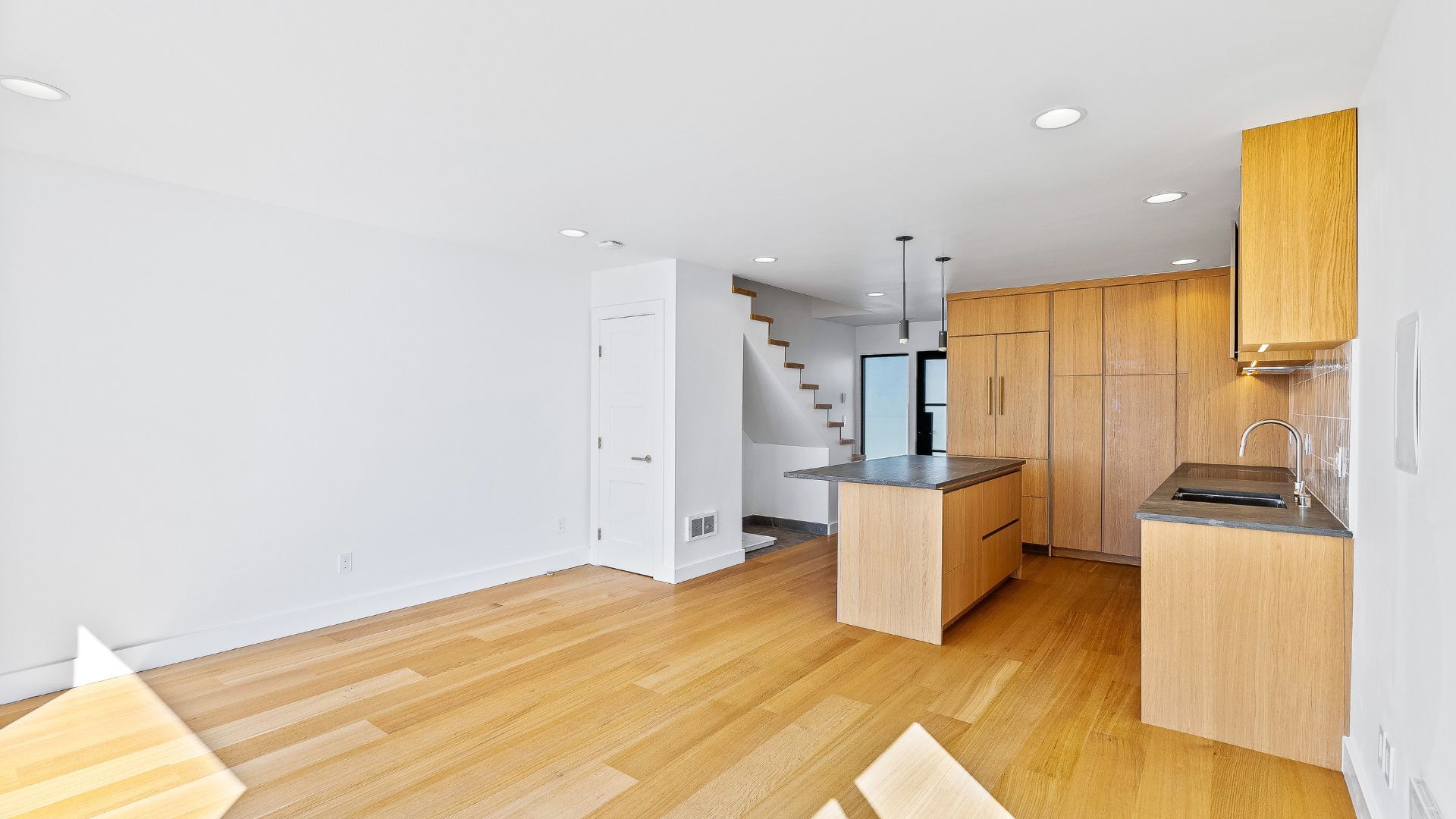 Bright modern kitchen and living area with wood floors, white walls, and wood cabinets