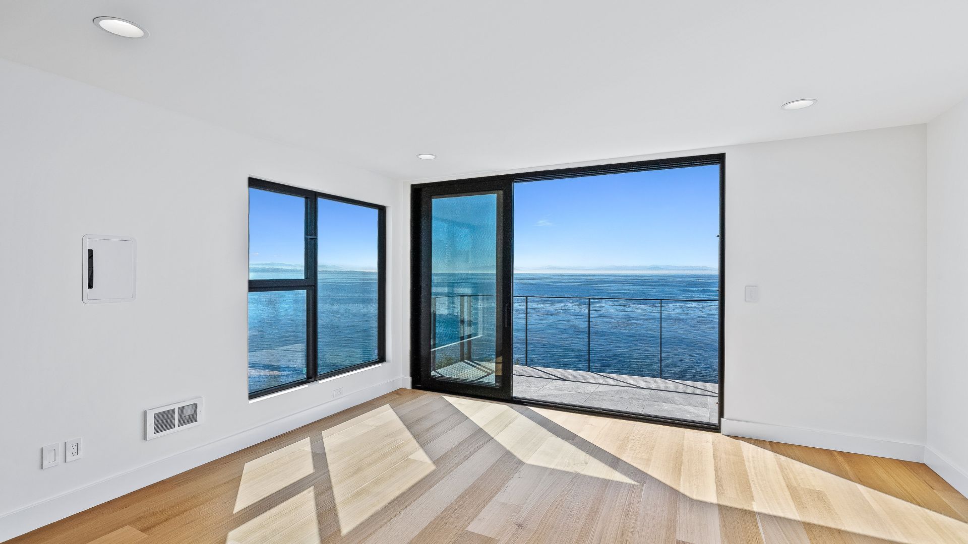 Bright empty room with wood floors and large windows overlooking the ocean and city skyline