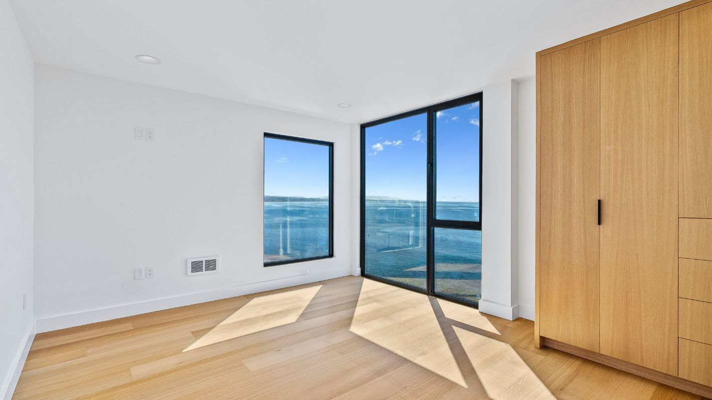 Bright empty room with floor-to-ceiling windows, city view, and light wood flooring.