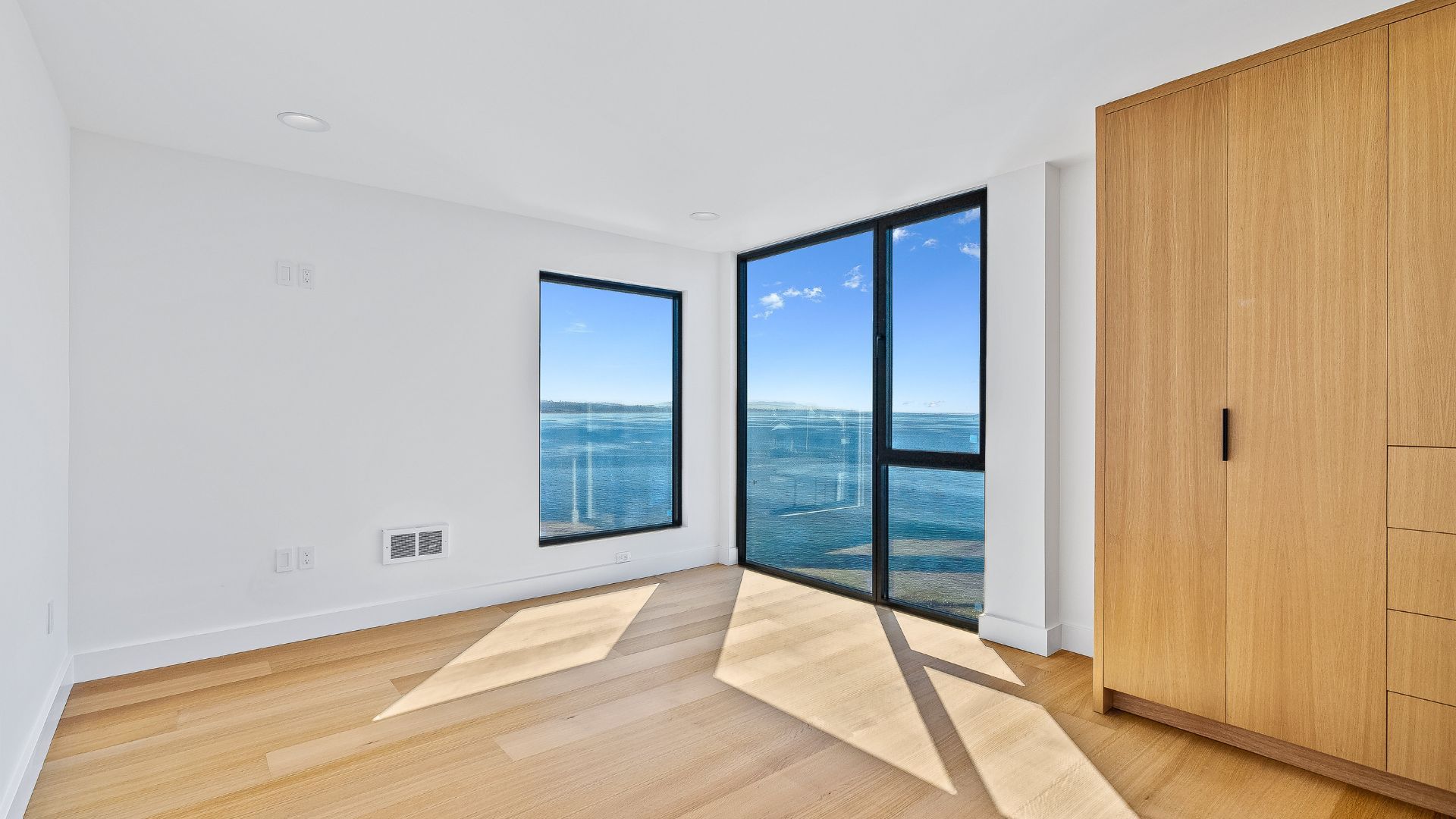 Bright empty room with wood floor, large windows, and ocean view.