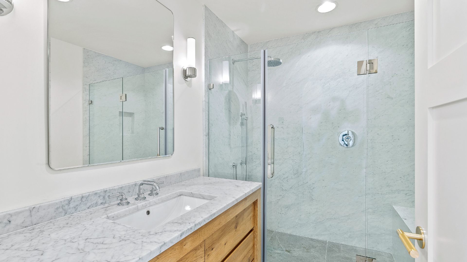 Bright white bathroom with marble vanity, large mirror, glass shower, and light blue tile accents