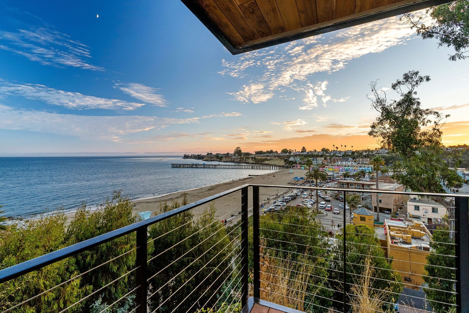 Balcony view of a coastal city at sunset, with ocean, shoreline, and railing in the foreground