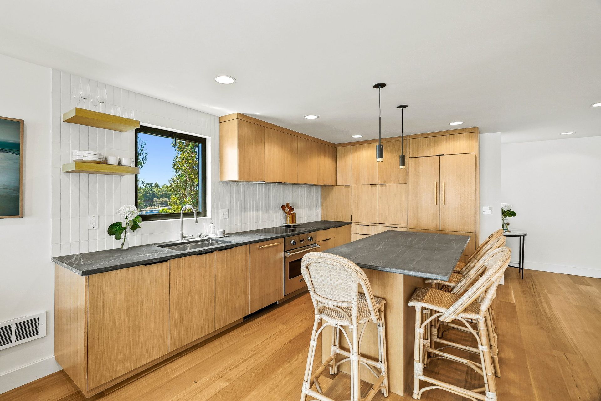 Bright modern kitchen with wood cabinets, granite island, and wicker bar stools