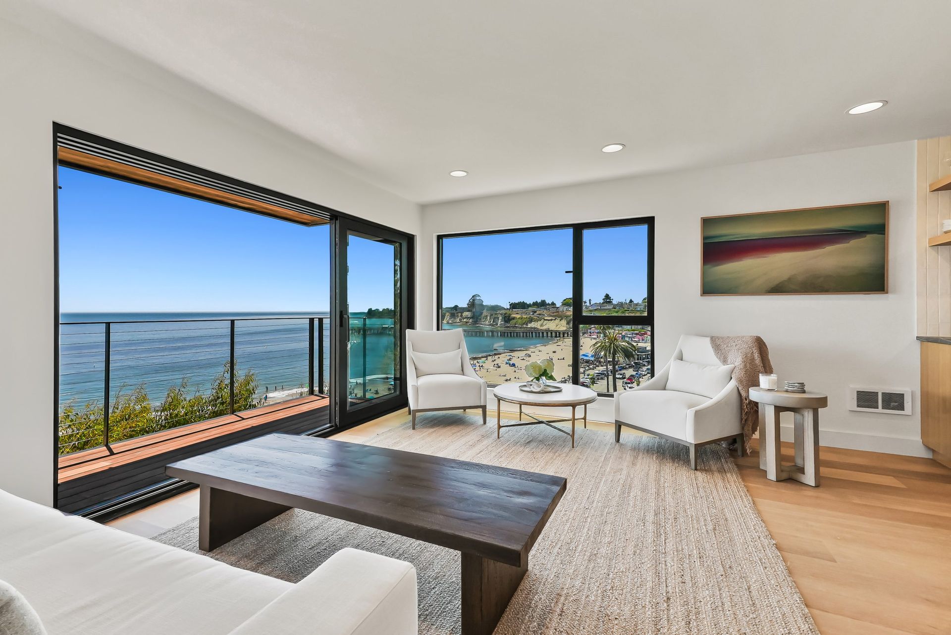 Bright living room with ocean views, white chairs, dark coffee table, and large glass doors opening to a balcony.