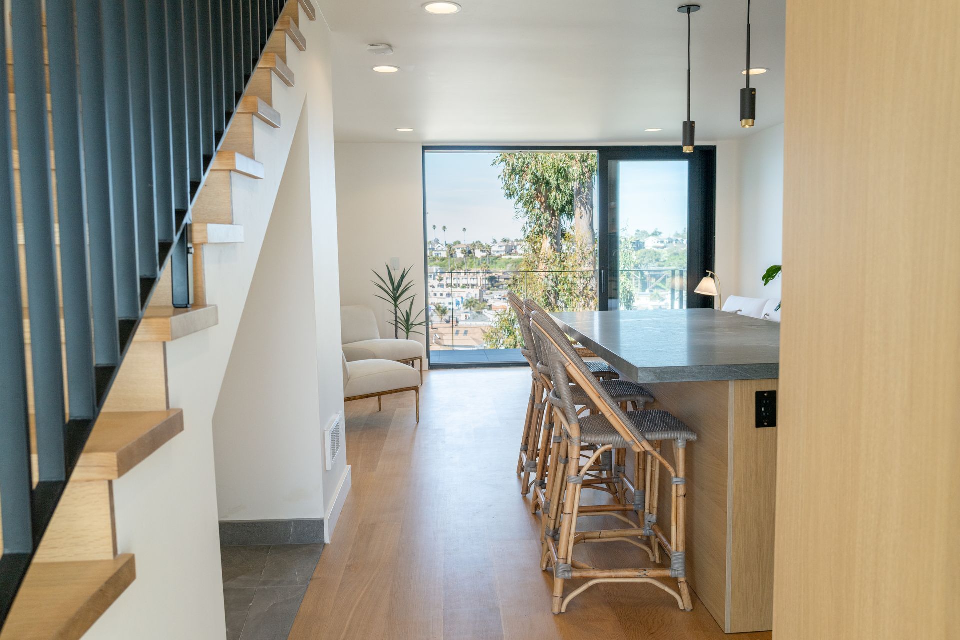 Modern kitchen and dining area with staircase, island stools, and large glass doors opening to a view