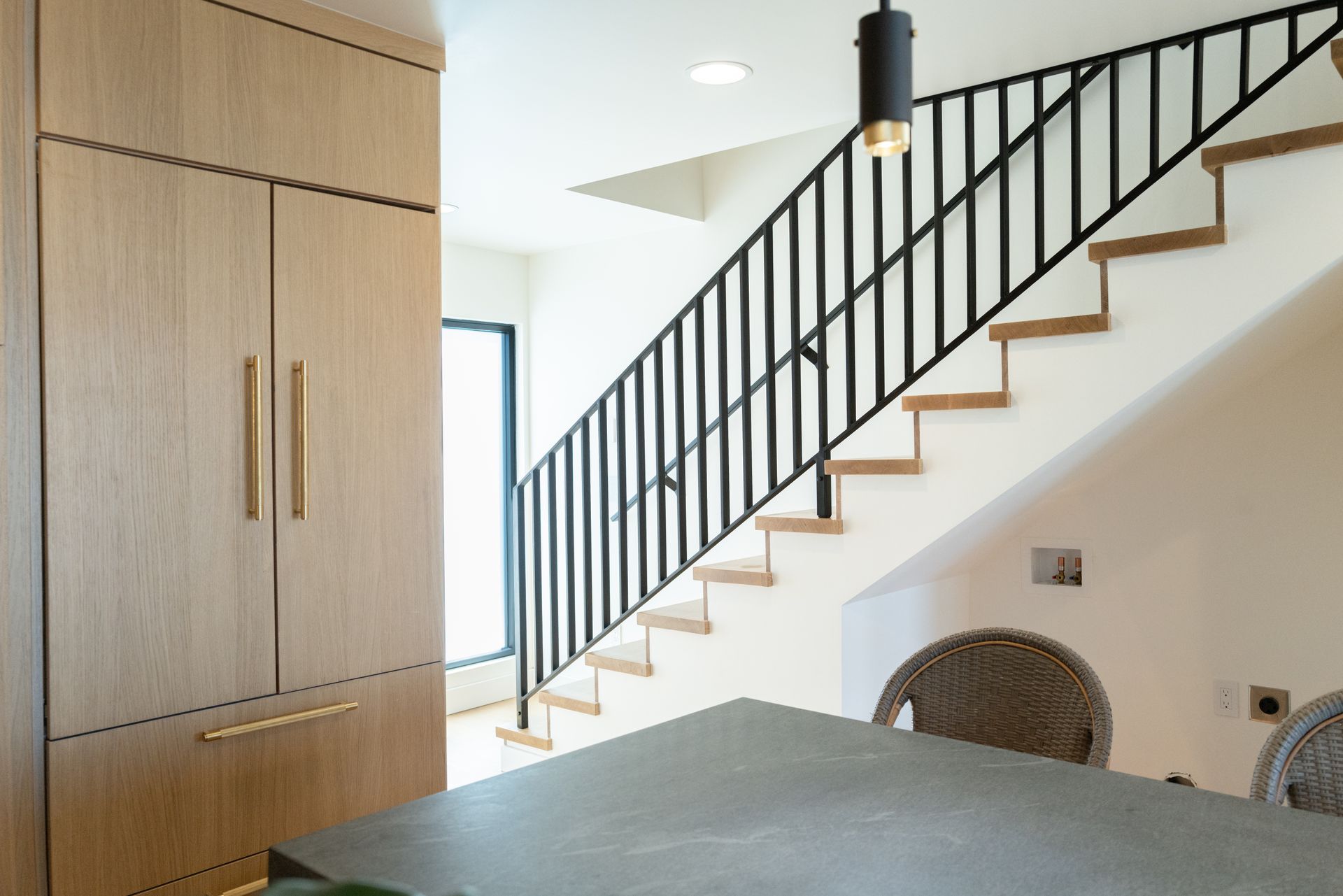 Modern interior with staircase, black railing, light wood cabinets, and a dining table in the foreground