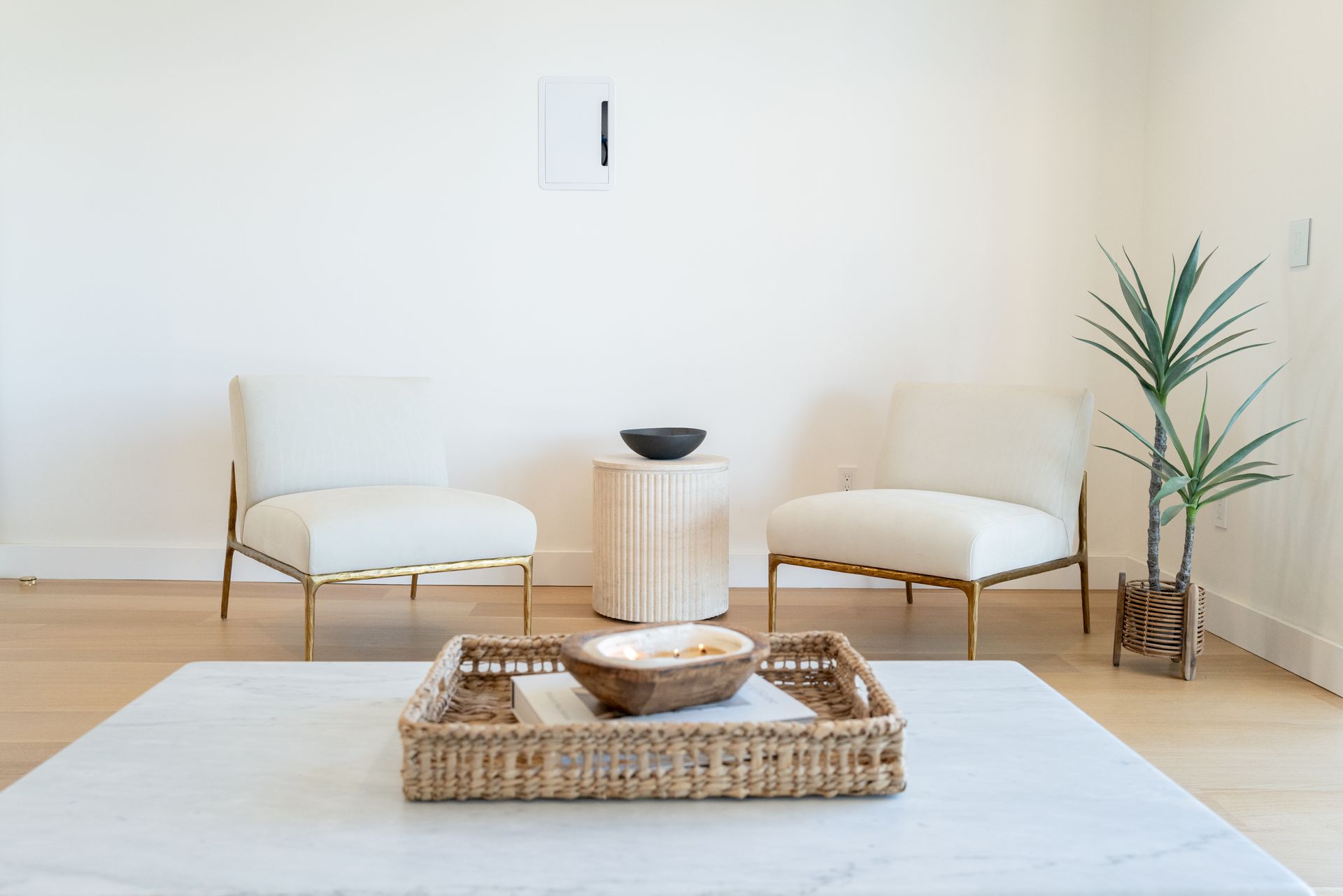 Minimalist living room with white chairs, woven tray table, and a potted plant.