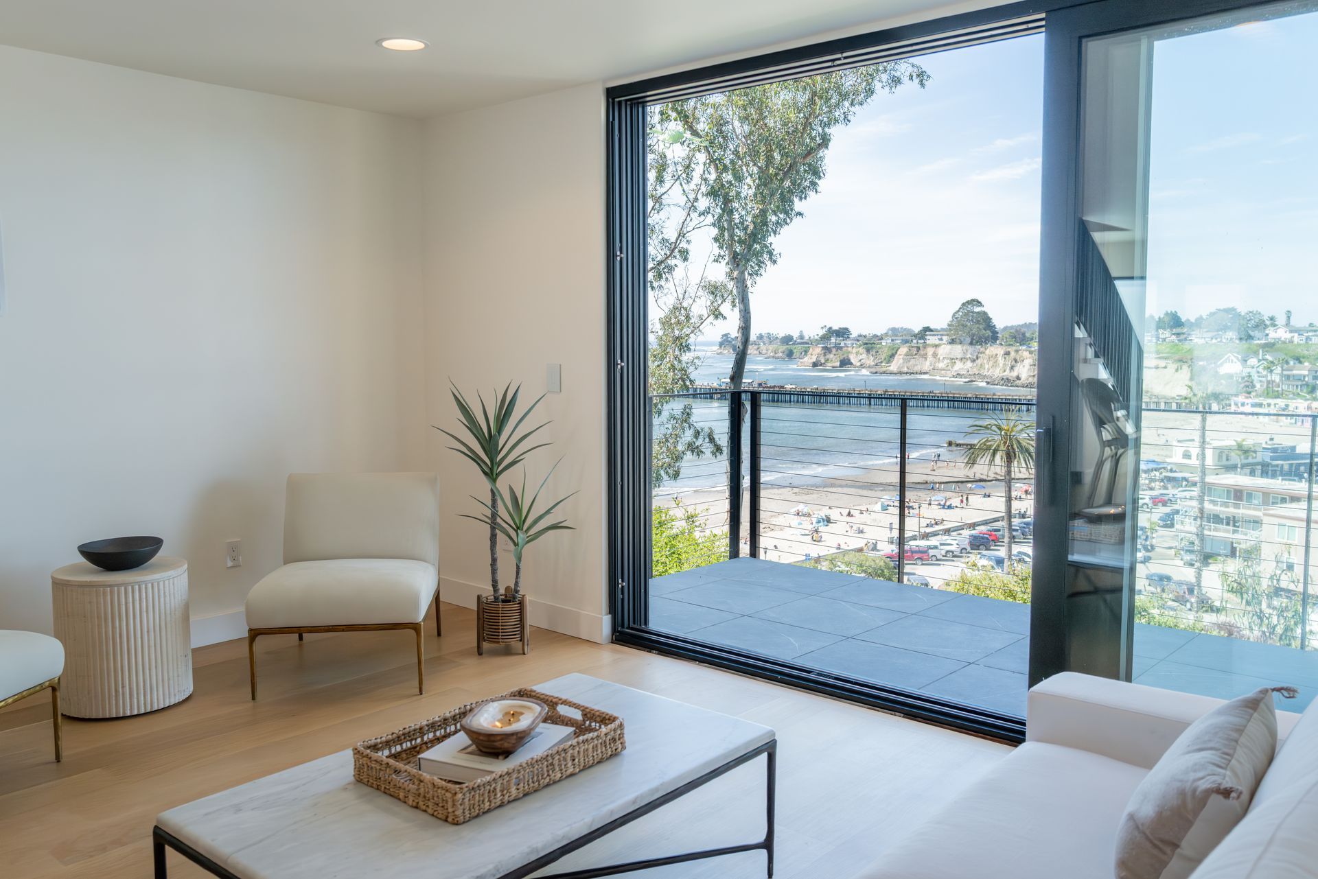 Bright modern living room with white chairs, wood floors, and a large ocean-view sliding glass door