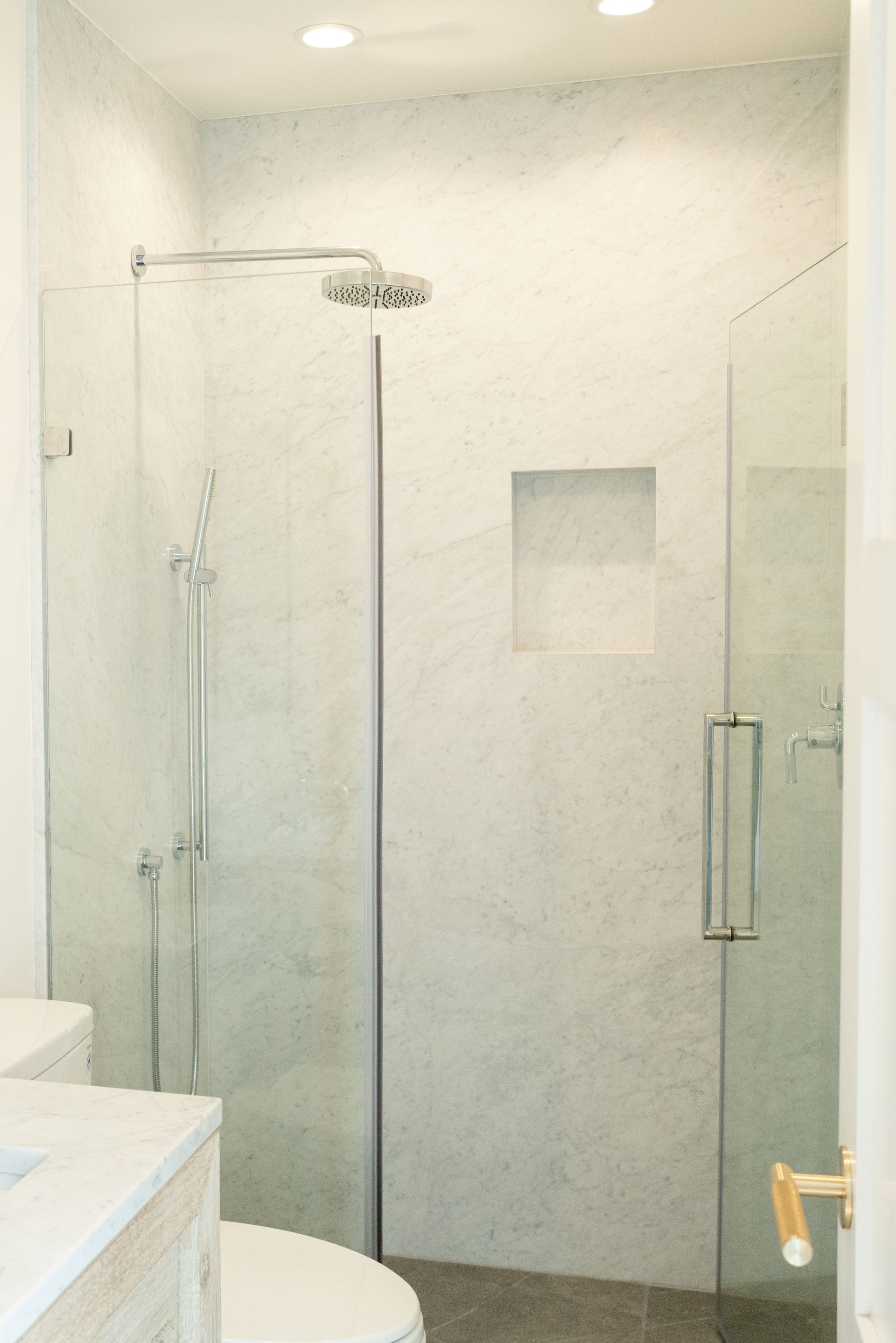 Modern white bathroom with glass shower, wall niche, and toilet partially visible