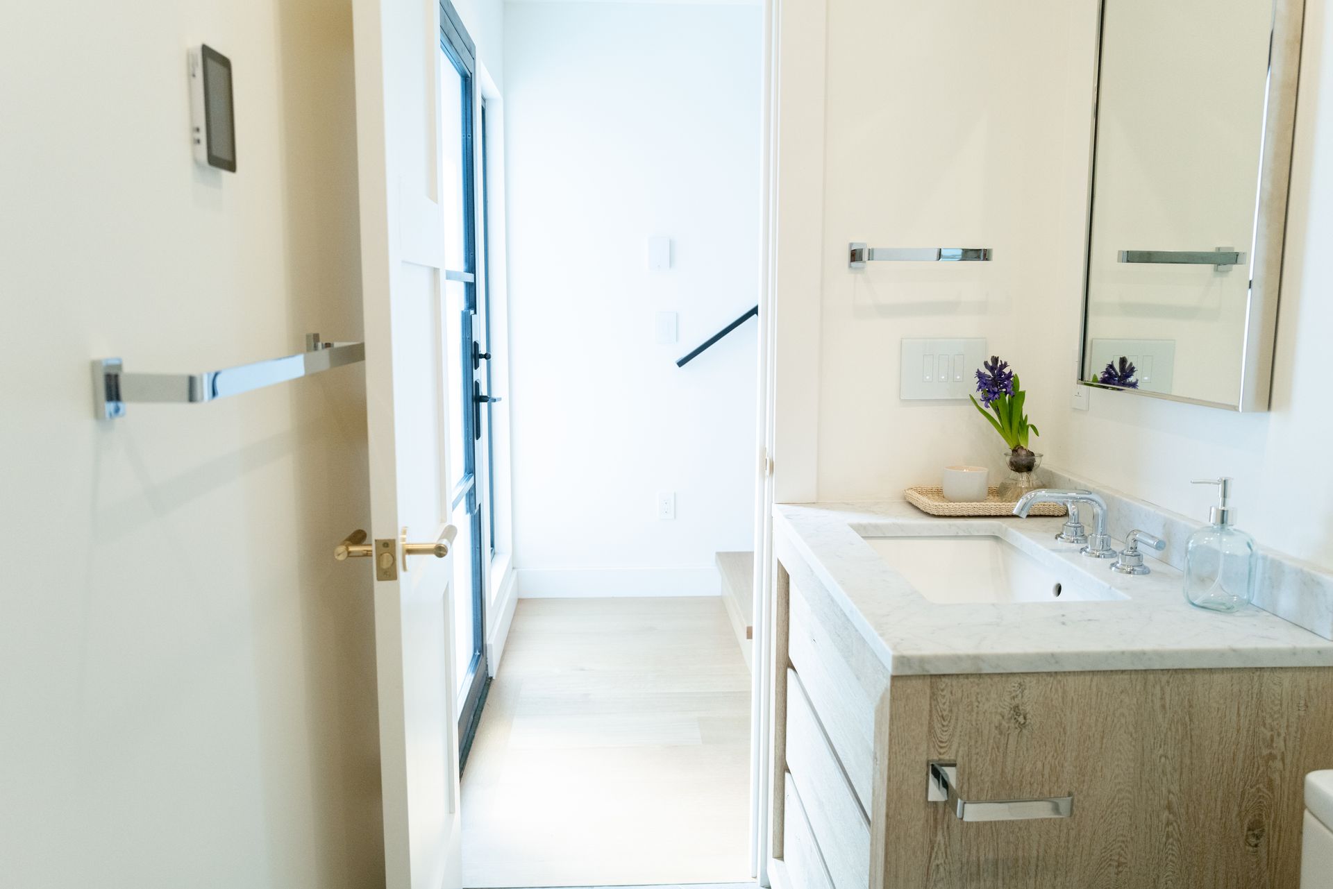 Bright bathroom vanity with mirror, sink, and vase of flowers; hallway visible through open door
