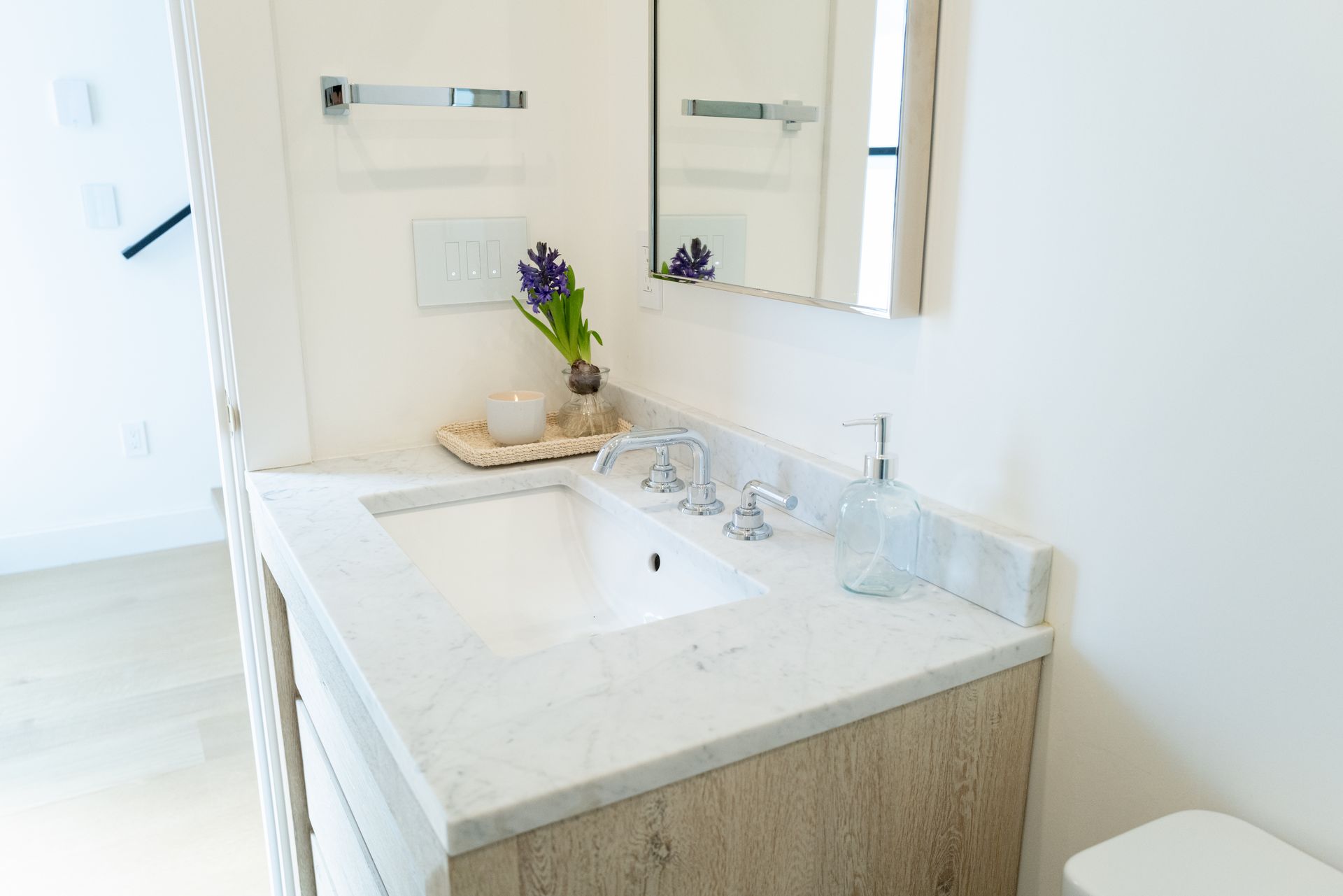 Bright bathroom vanity with white countertop, sink, mirror, and flower vase near a window